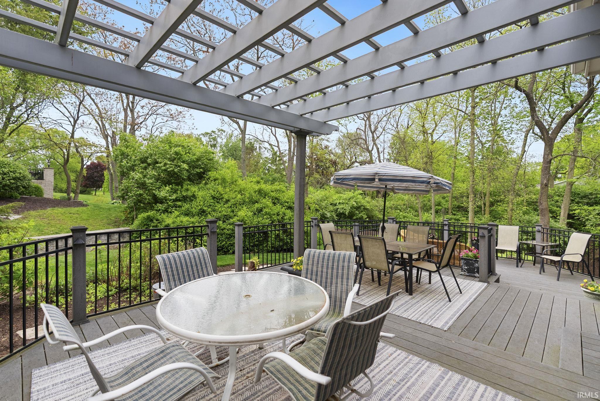 Expansive rear deck featuring a composite wood-finish surface, a louvered pergola, and black iron railings