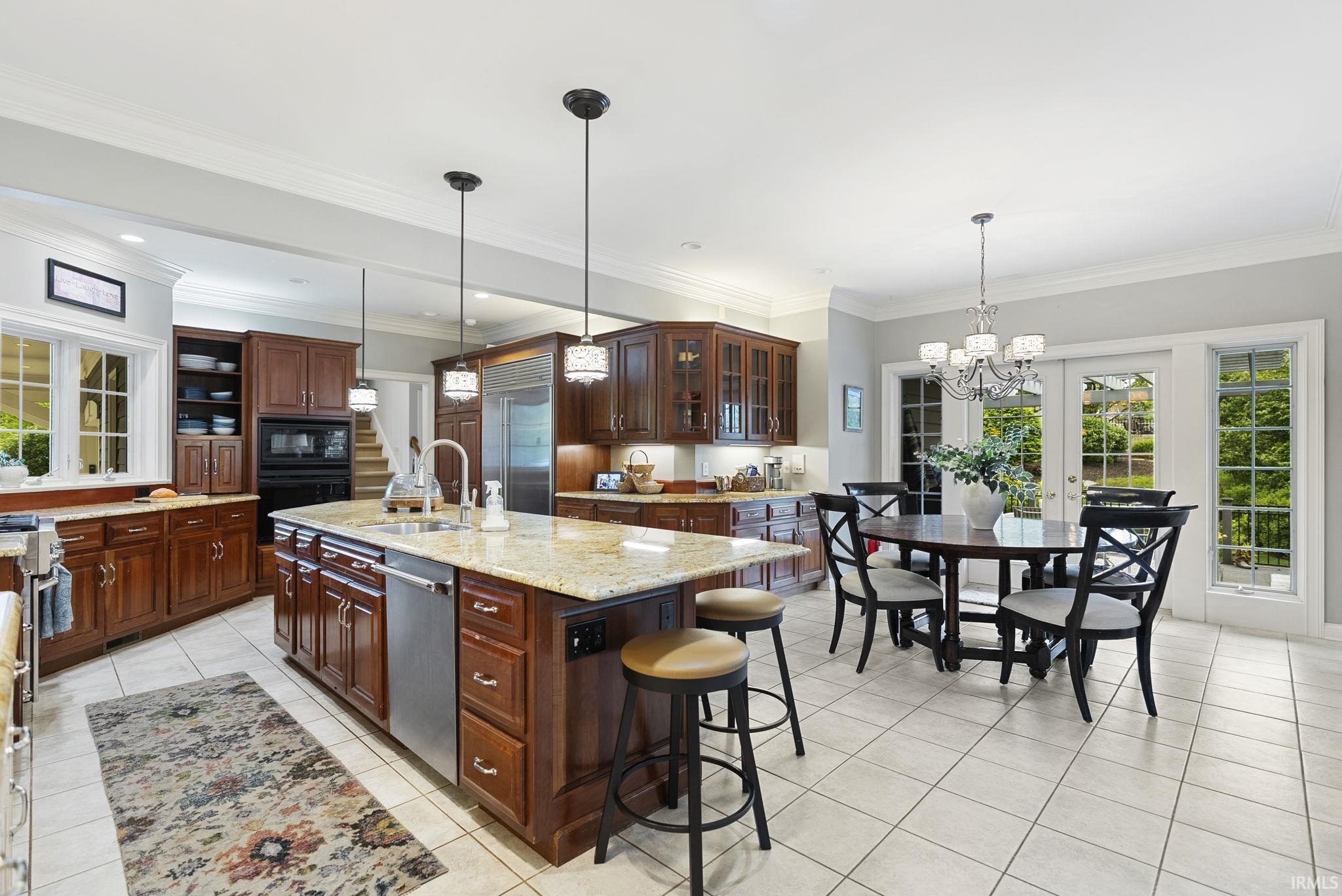 Spacious kitchen featuring rich wood cabinetry, light granite countertops, stainless steel appliances, a large center island with integrated sink, and white tile flooring
