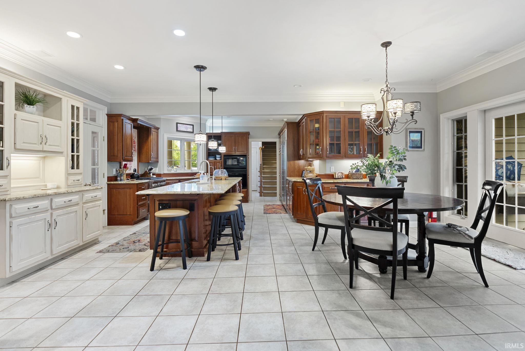 Spacious kitchen featuring a large central island with seating, a mix of stained wood and painted cabinetry, light-toned tile flooring, recessed lighting, and crown molding