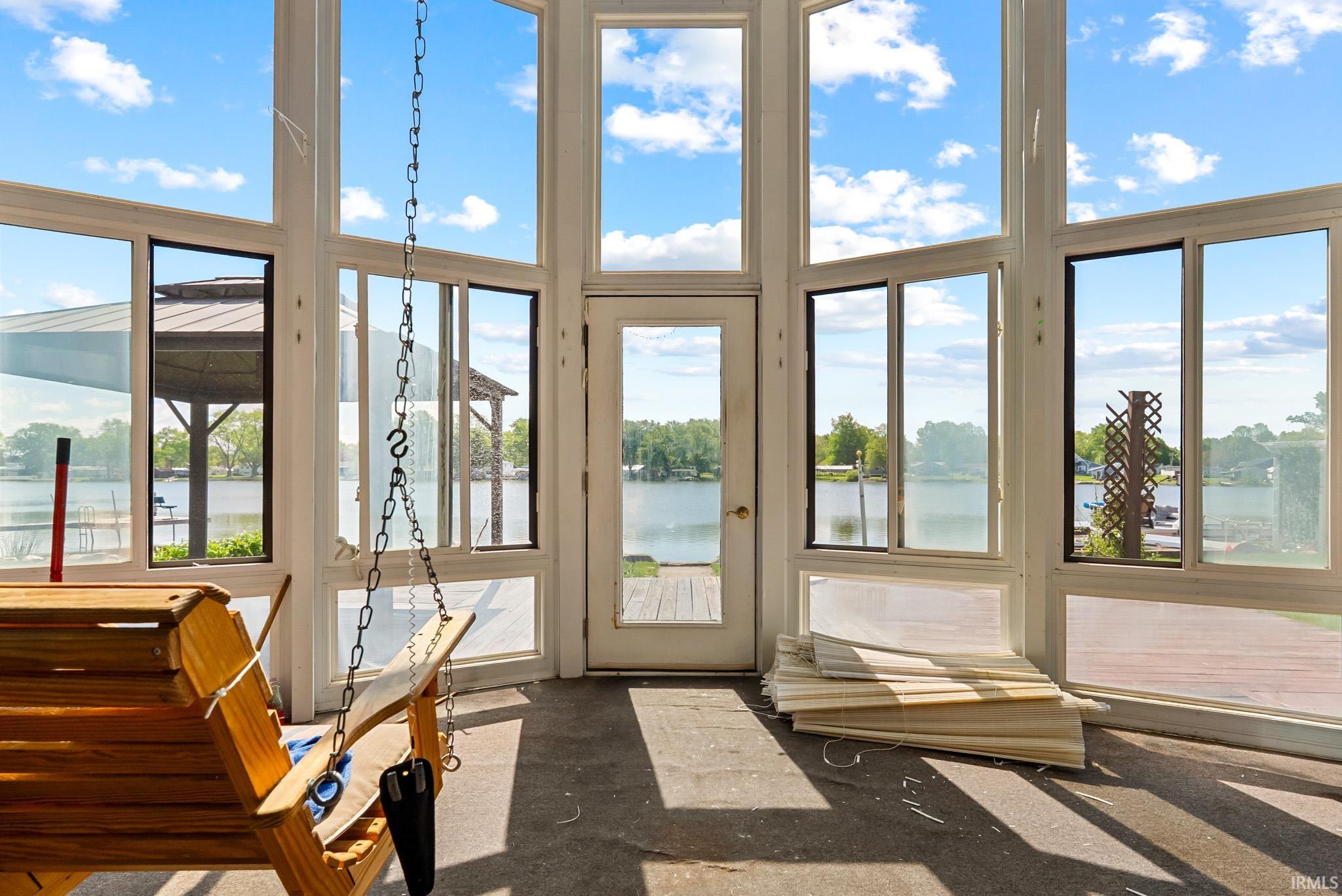 Expansive sunroom featuring numerous floor-to-ceiling windows, a glass-paneled exterior door, and direct water frontage