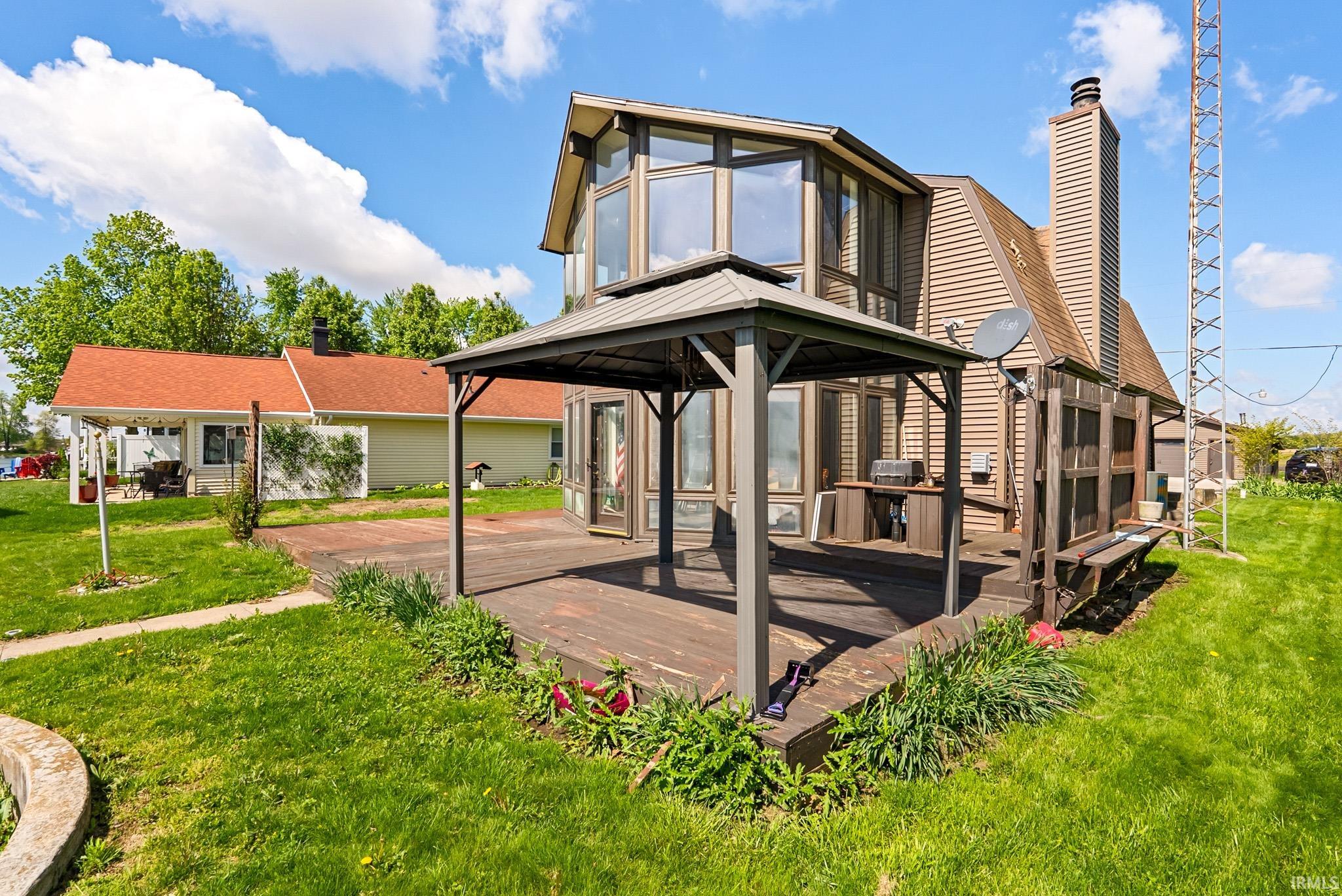 Expansive multi-level wood deck featuring a covered gazebo, built-in outdoor kitchen area, and integrated bench seating