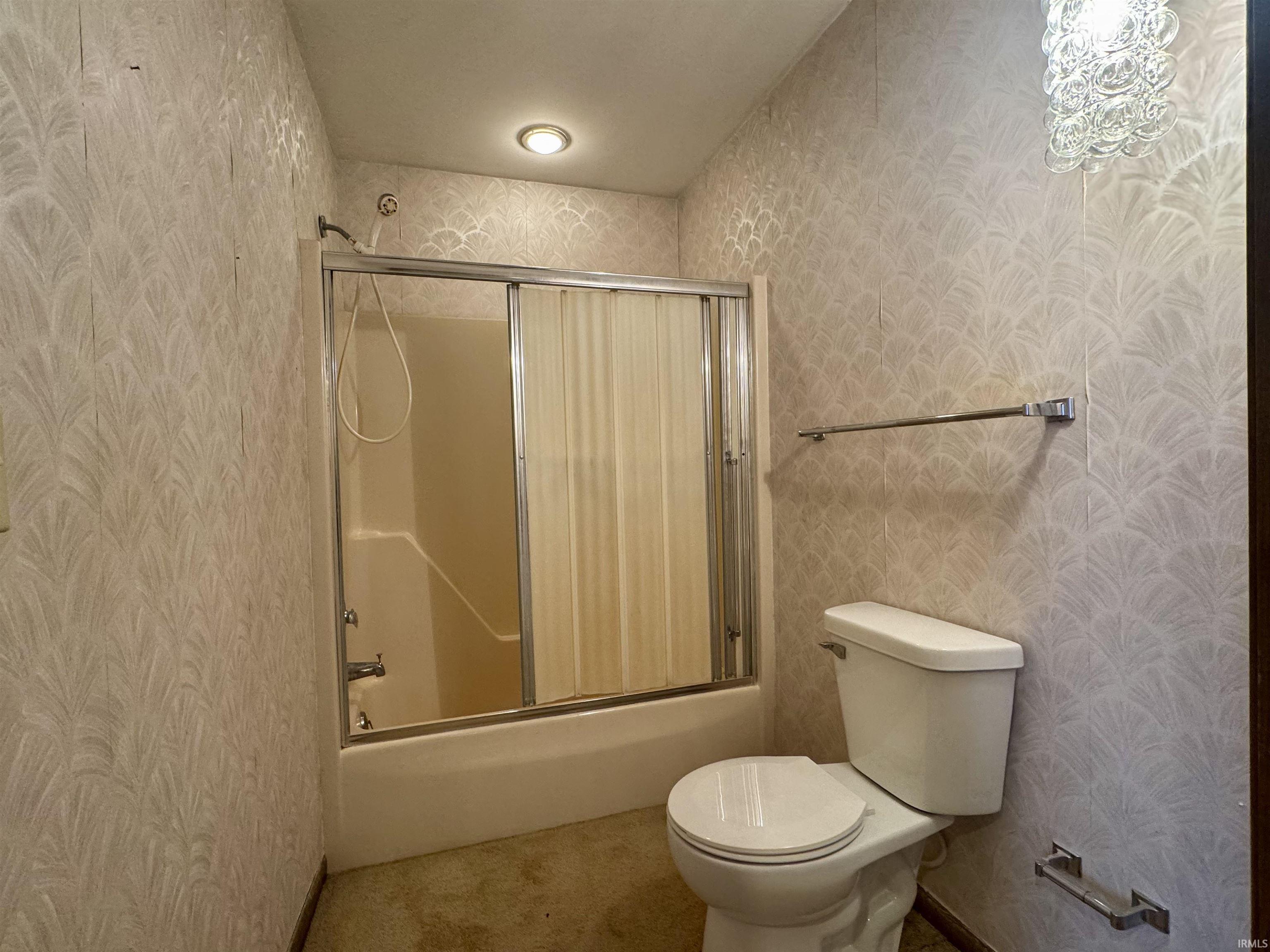 Bathroom featuring a shower/tub combination with sliding glass doors, a white toilet, recessed ceiling lighting, and a decorative wall sconce