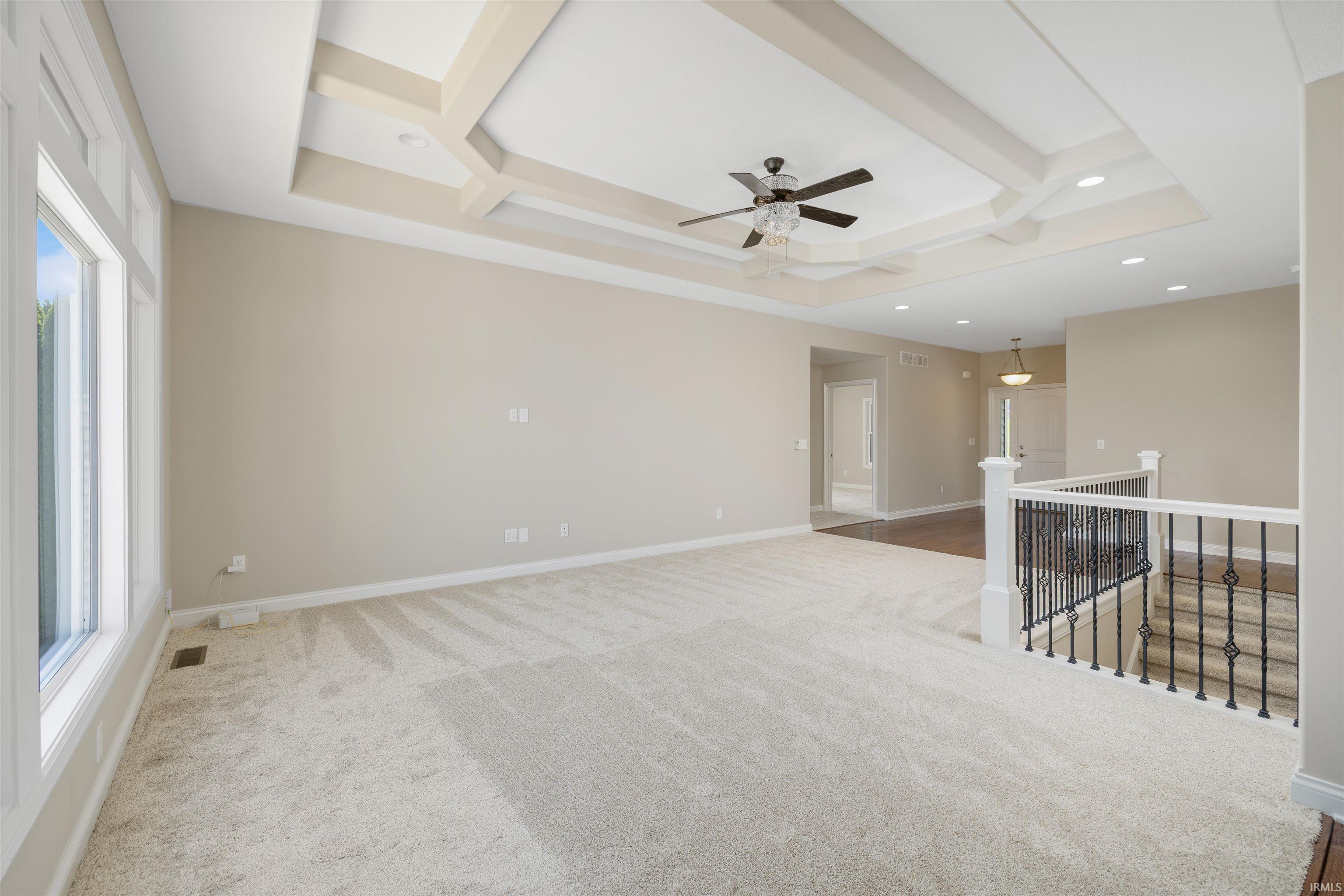 Spacious room featuring a decorative coffered ceiling with a ceiling fan, recessed lighting, expansive windows, and plush carpeting