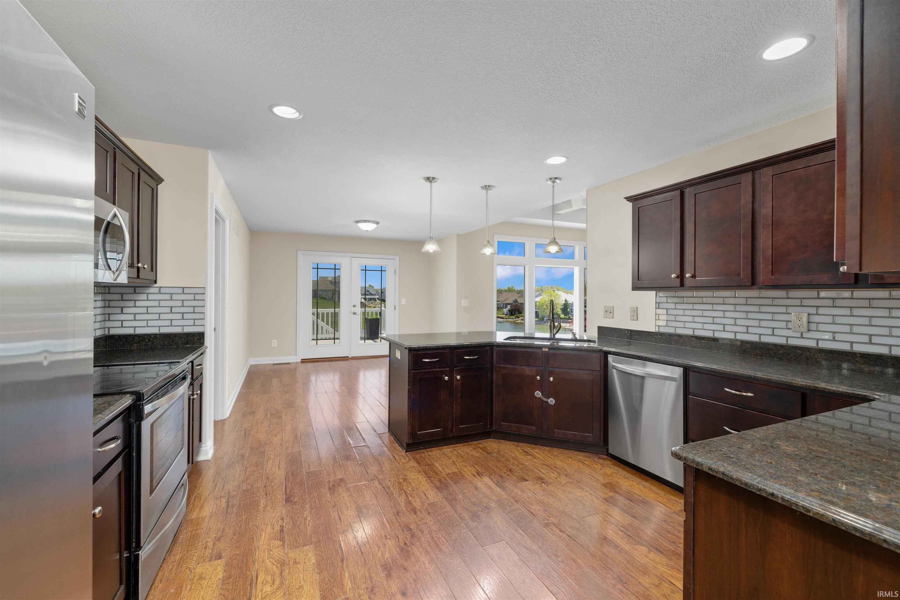 Open-concept kitchen featuring dark wood cabinetry, stainless steel appliances, dark countertops, a tiled backsplash, and wood-finish flooring