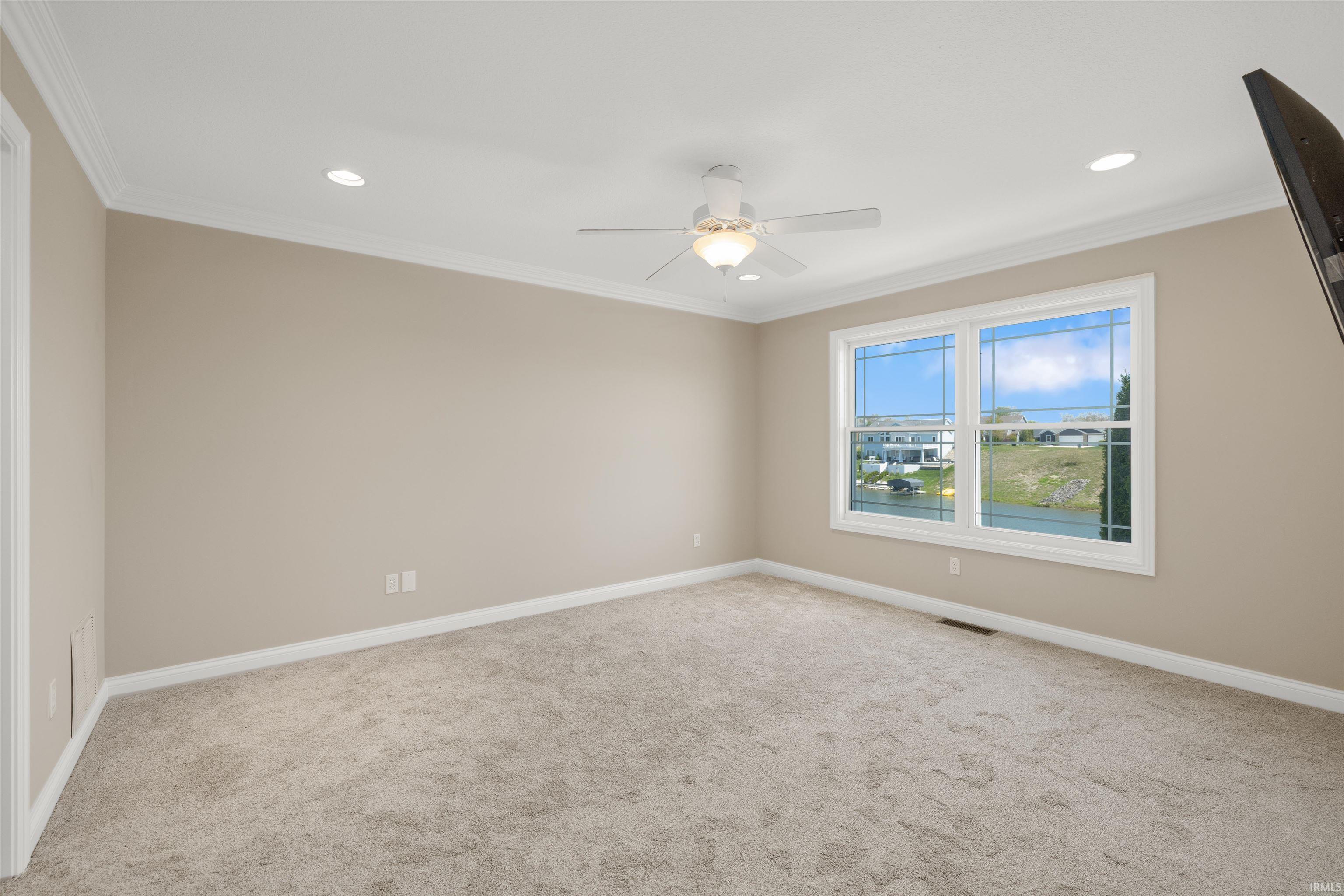 Spacious room featuring neutral carpeting, light beige walls, white crown molding, and a ceiling fan with integrated lighting