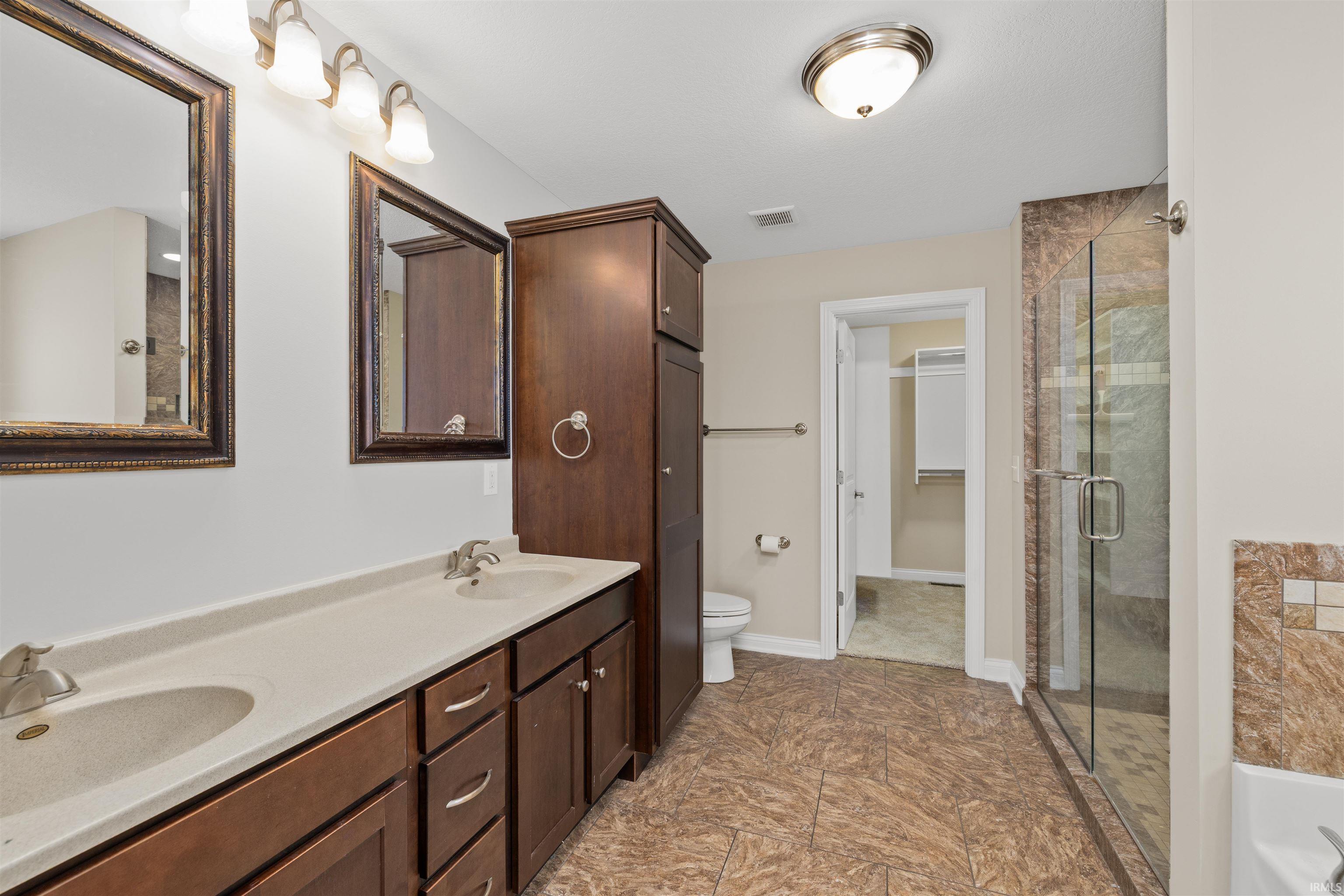 Double vanity featuring two undermount sinks, a tall linen cabinet, a glass-enclosed shower, and a built-in toilet