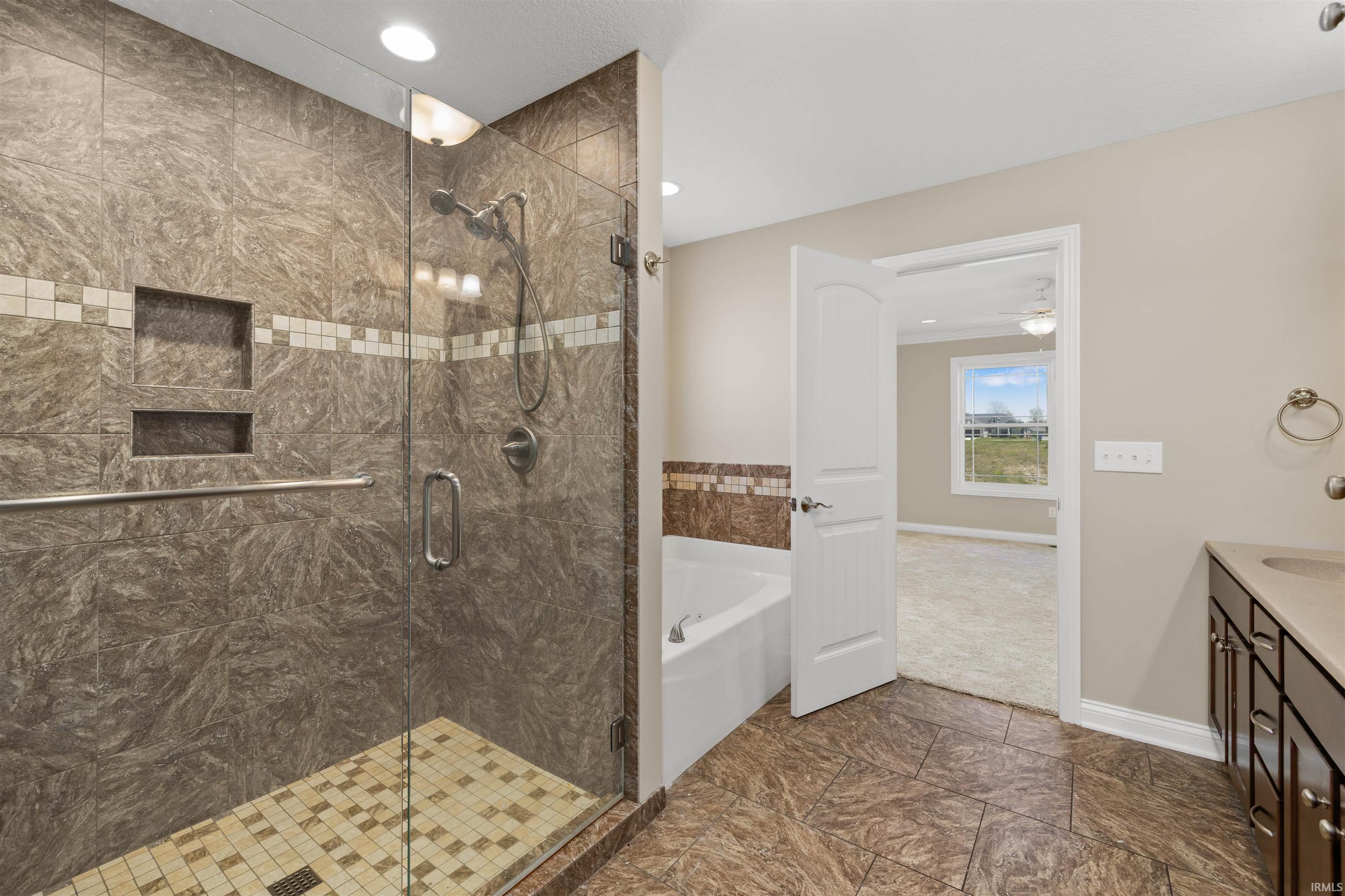 Spacious bathroom featuring a glass-enclosed shower with brown and cream tile, an integrated shower niche, and a separate soaking tub