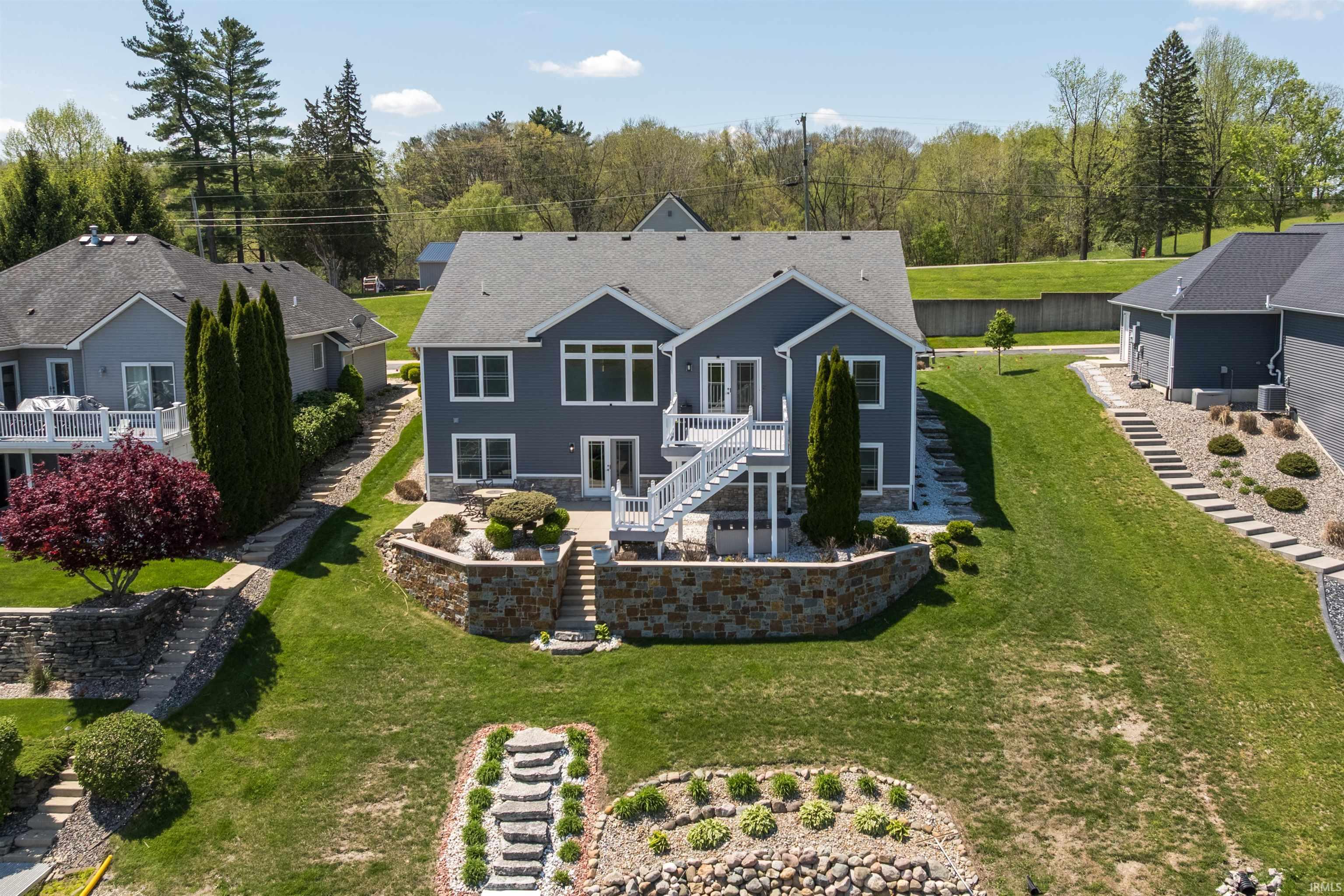 Expansive rear exterior featuring a multi-level deck with white railings, a stone retaining wall, and a terraced lawn