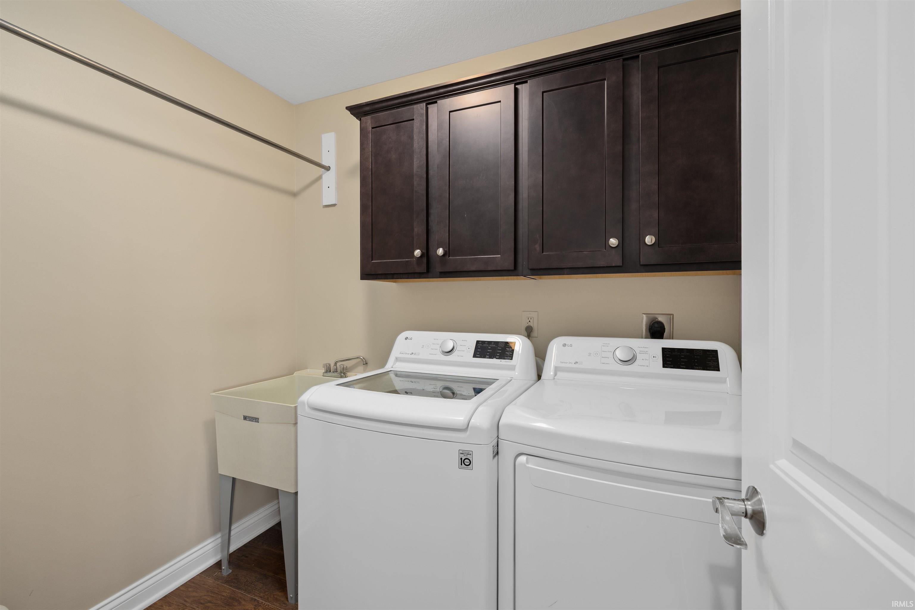 Dedicated laundry space featuring dark wood-finish cabinetry, a utility sink, and wood-finish flooring
