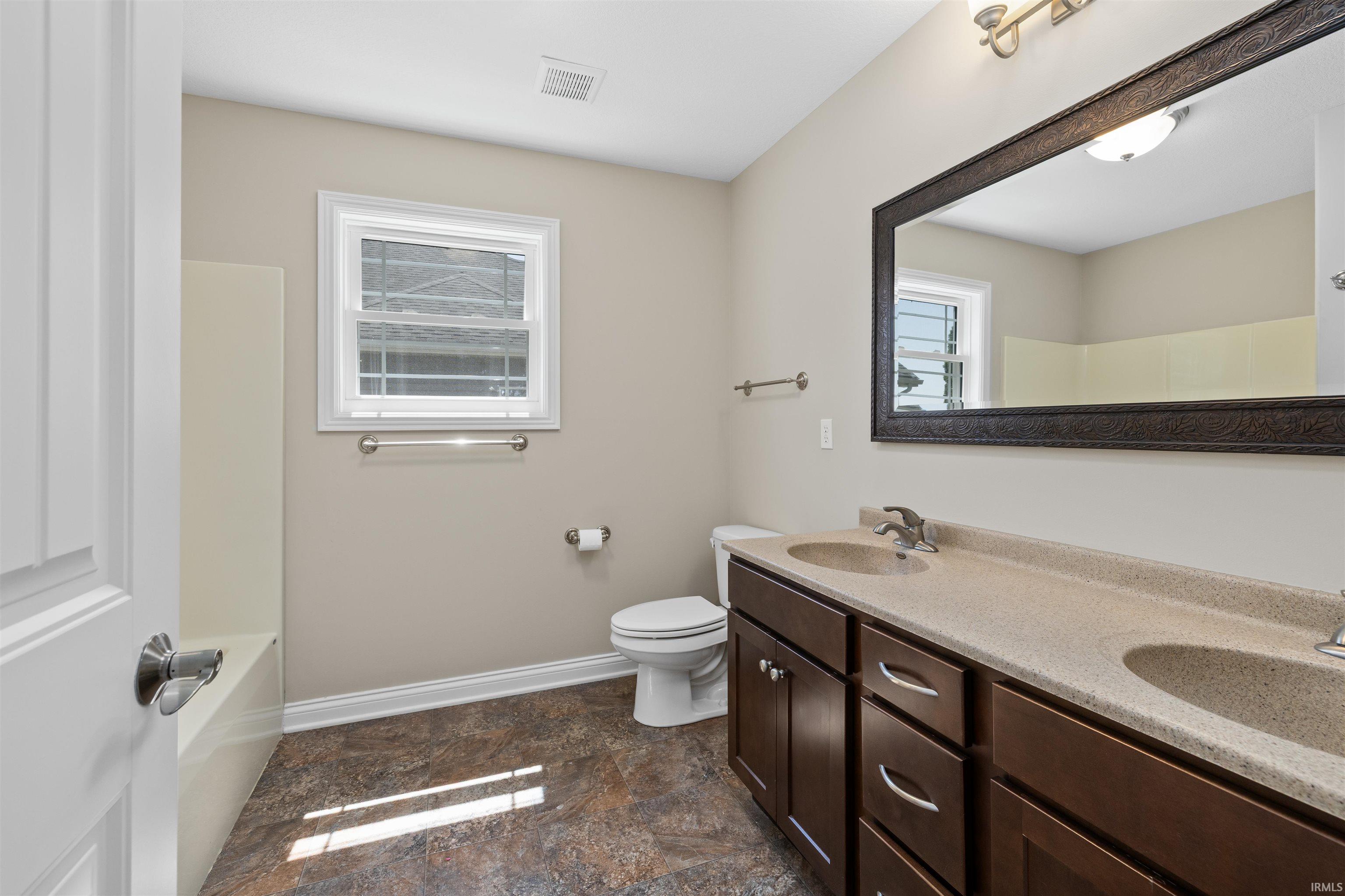 Bathroom featuring a double vanity with stone-finish countertops, dark wood cabinetry, and dual undermount sinks