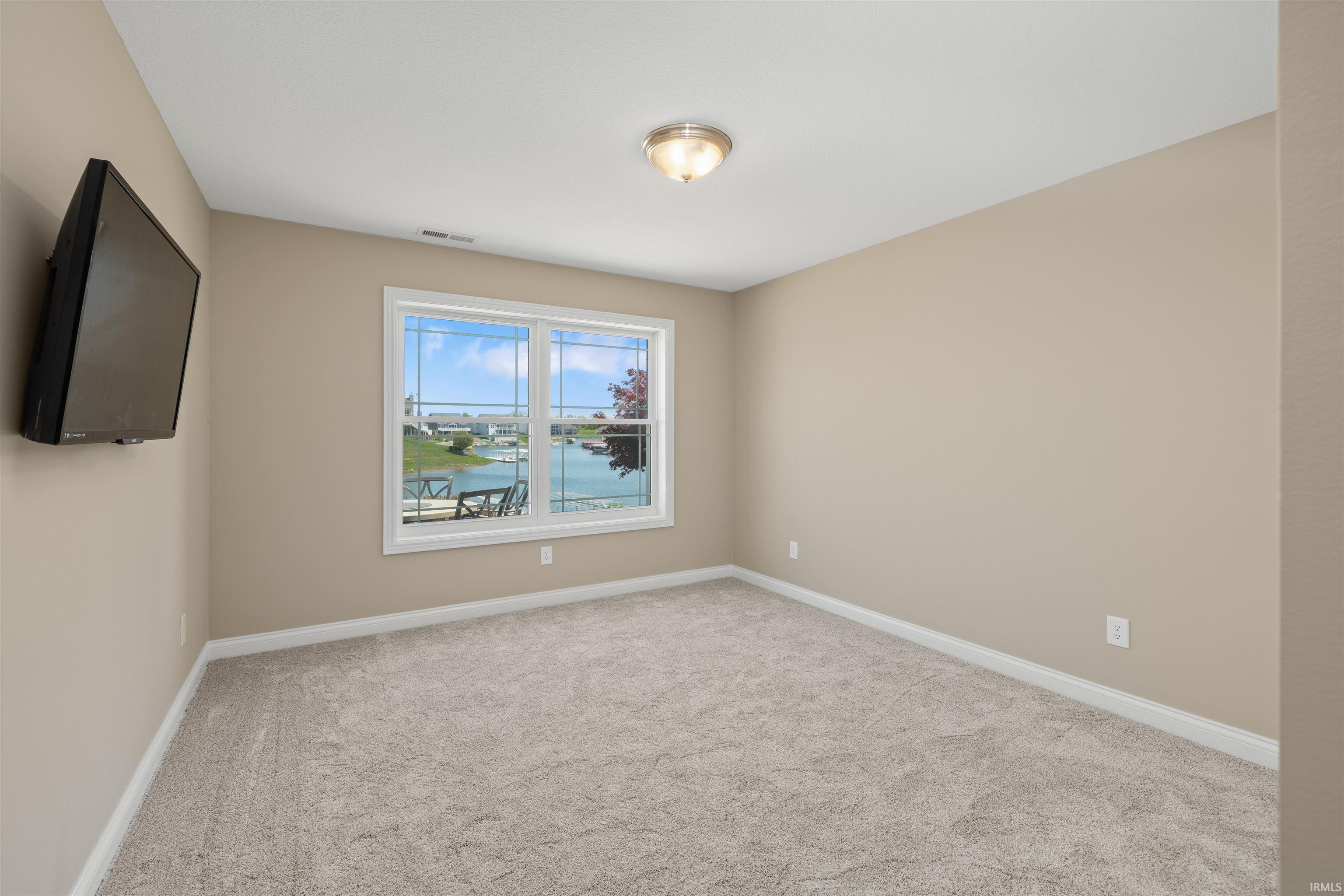 Spacious room featuring a large window overlooking a body of water, neutral carpet, light beige walls, white trim, and a flush mount ceiling light fixture