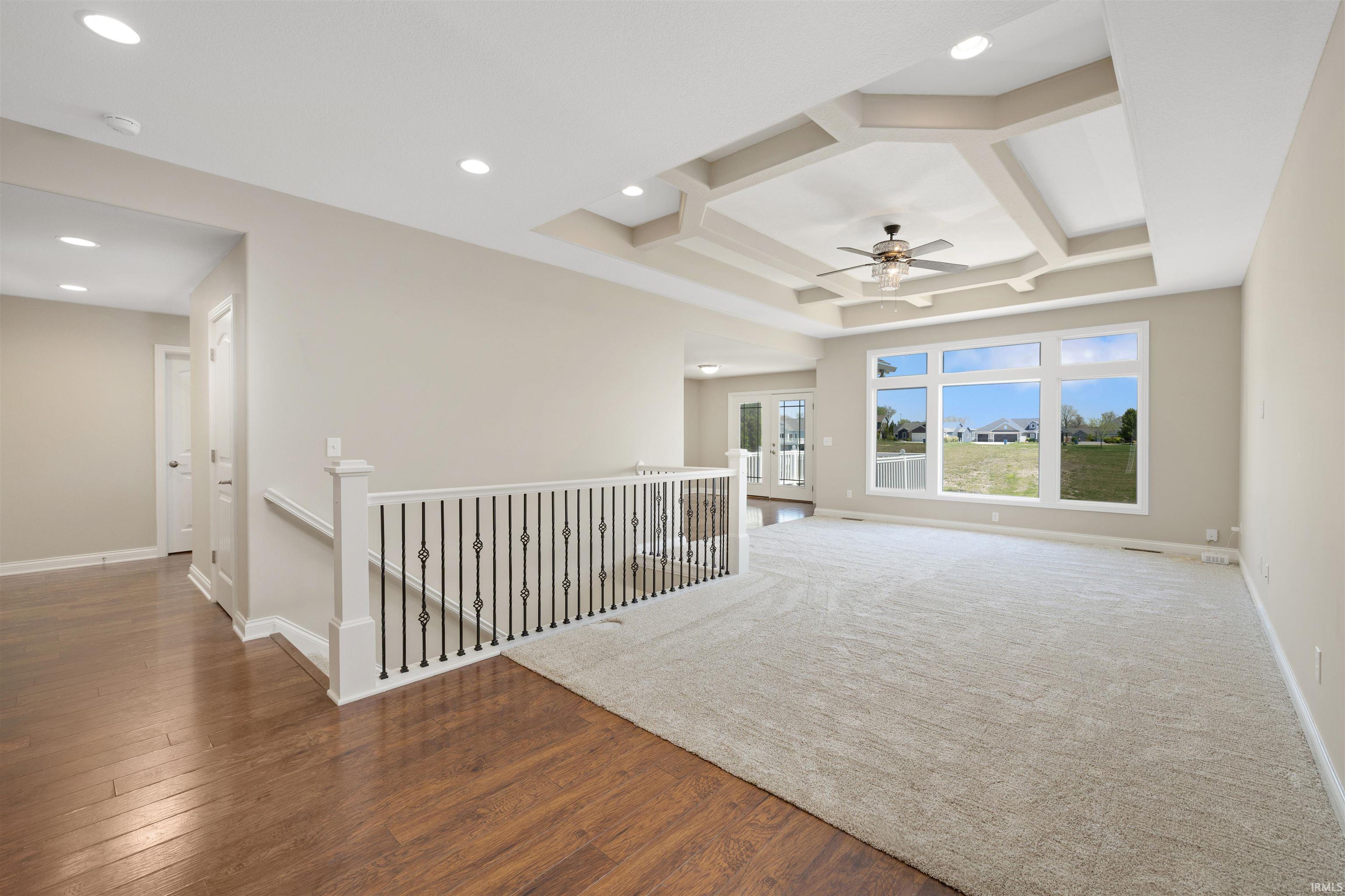 Expansive open concept living area featuring a decorative coffered ceiling with a ceiling fan, a large window array, and recessed lighting