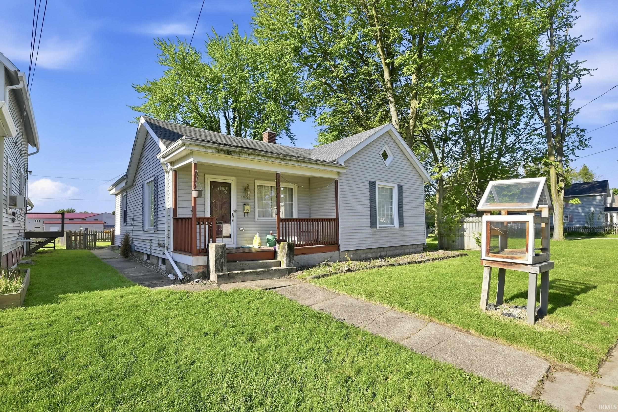 Single-story residence featuring light gray siding with white trim, a covered front porch with dark wood railings, and a concrete walkway leading to the entrance