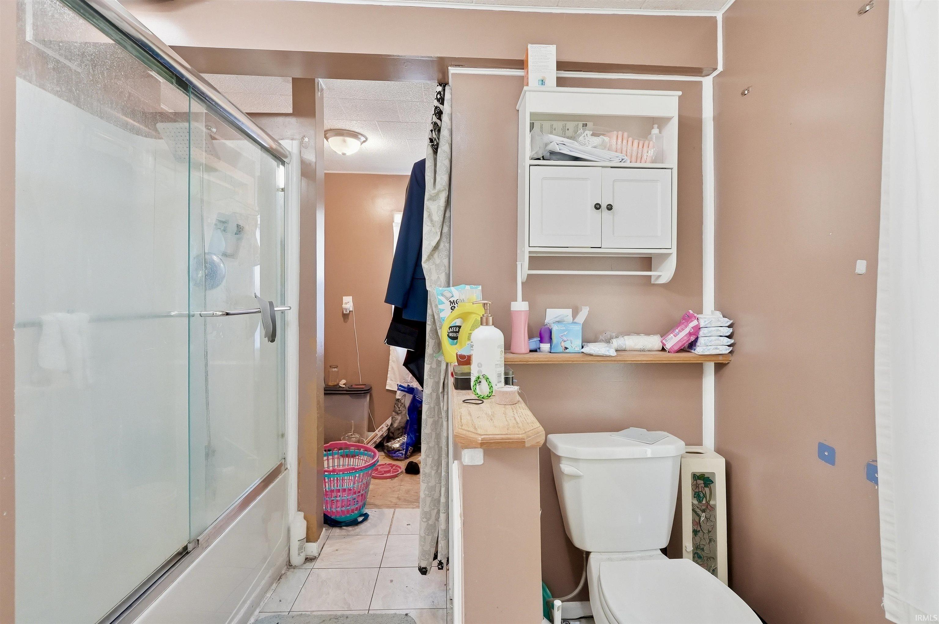 Bathroom featuring a shower with glass enclosure, white commode, and an integrated wall cabinet with open shelving