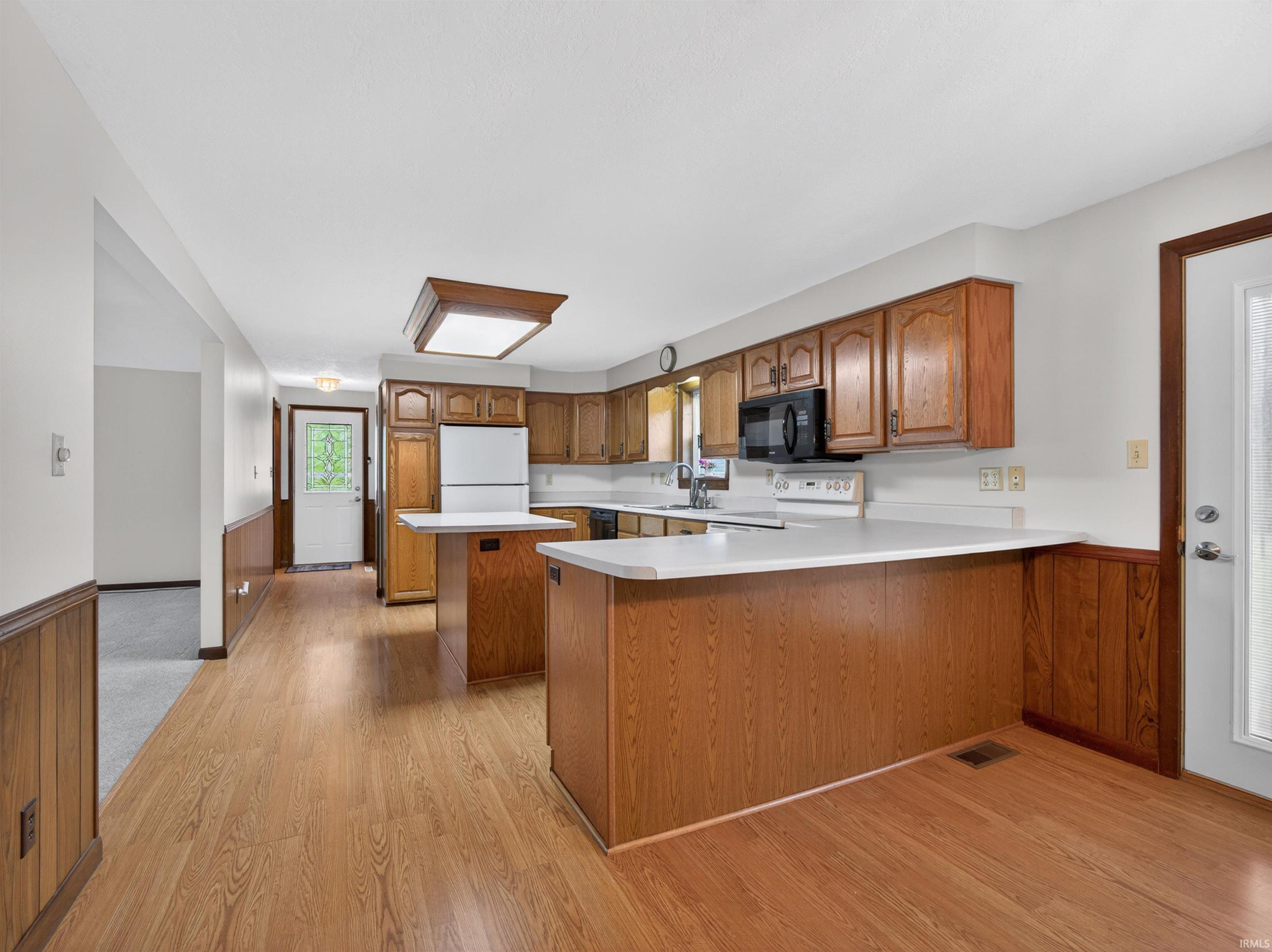 Kitchen featuring wood-finish flooring, wood cabinetry, white countertops, and white appliances
