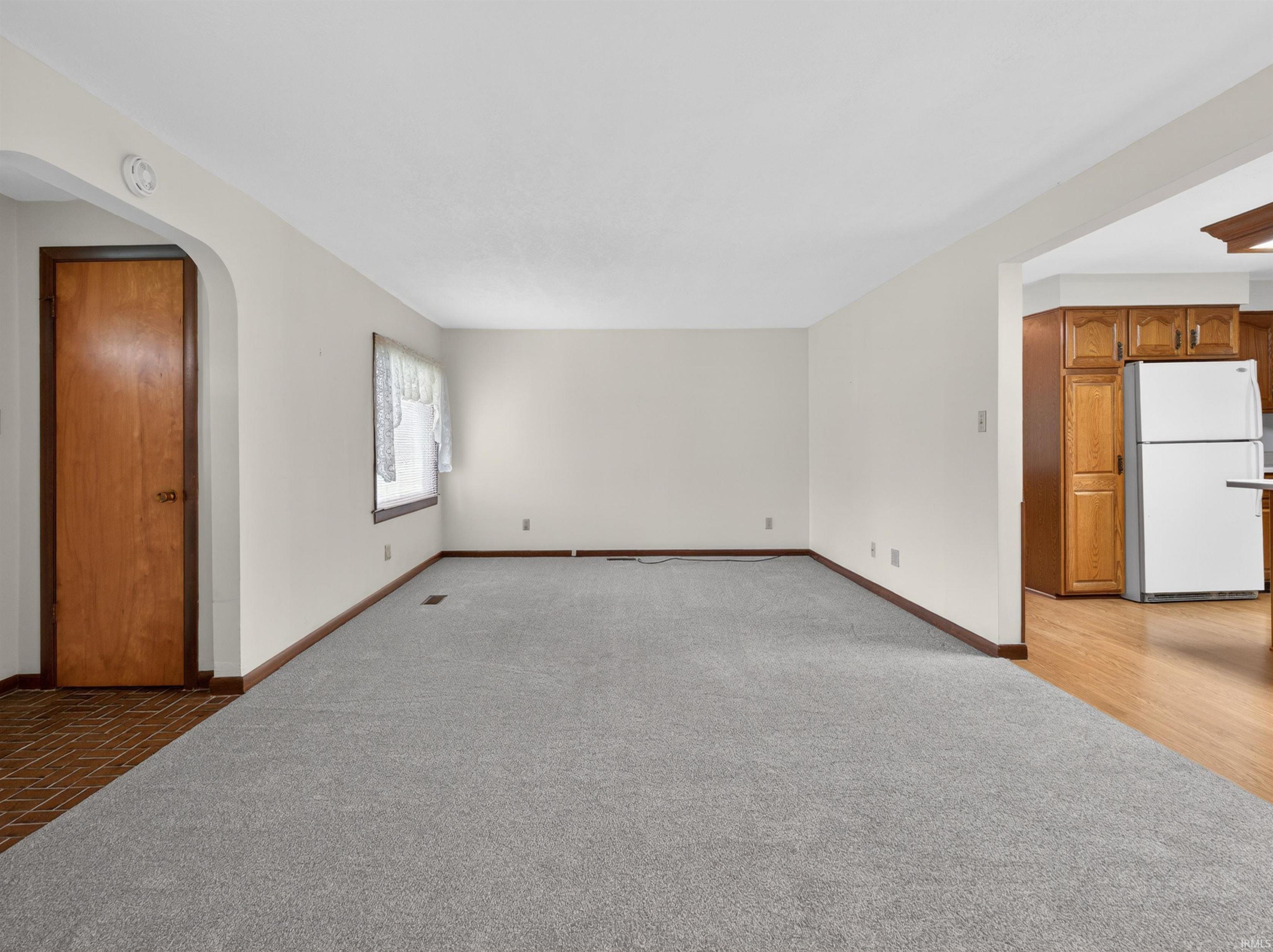 Spacious room with light neutral wall paint, gray carpet, and wood-finish baseboards