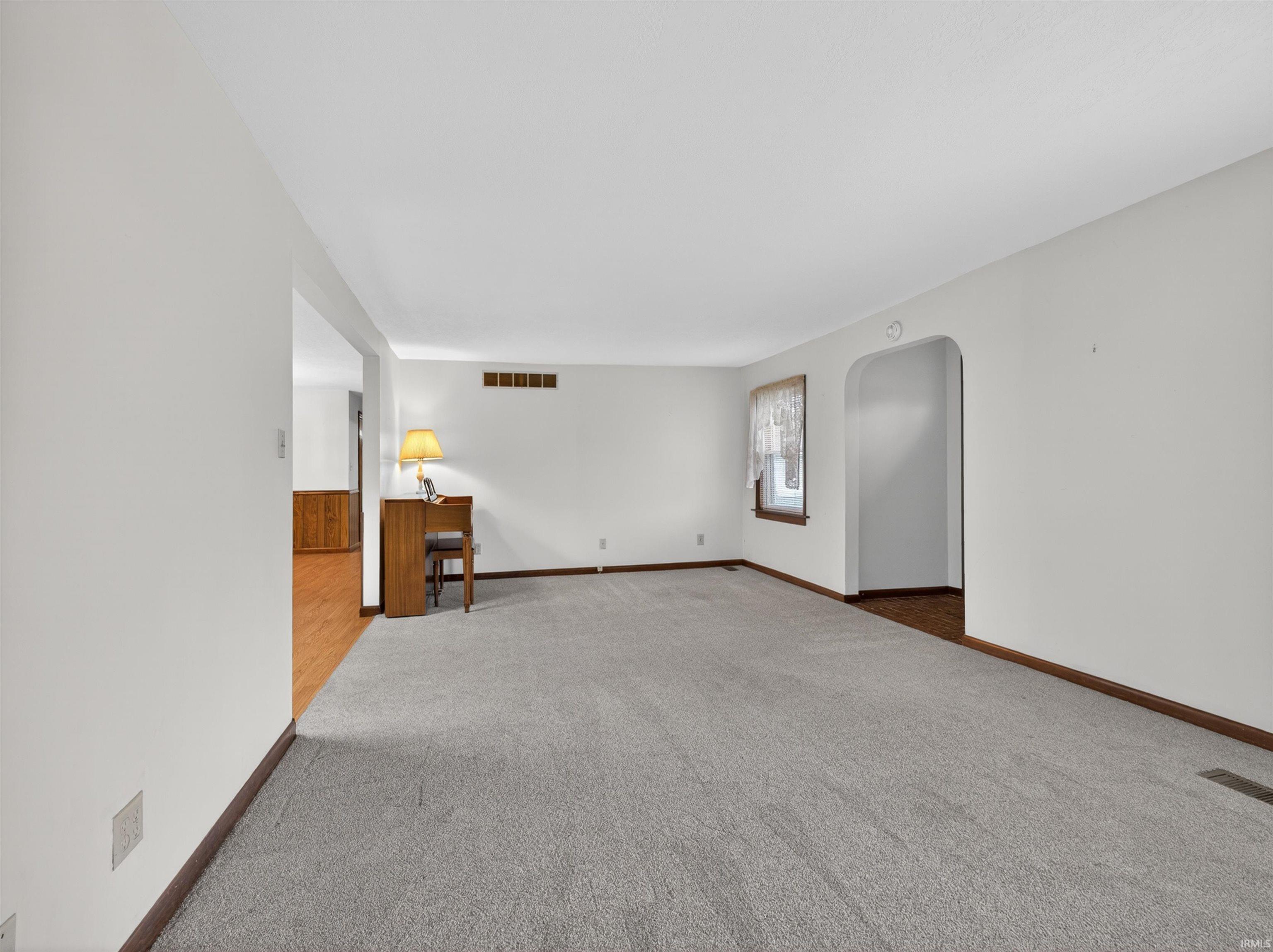 Spacious room featuring light gray carpeting, white walls, and dark wood-finish baseboards