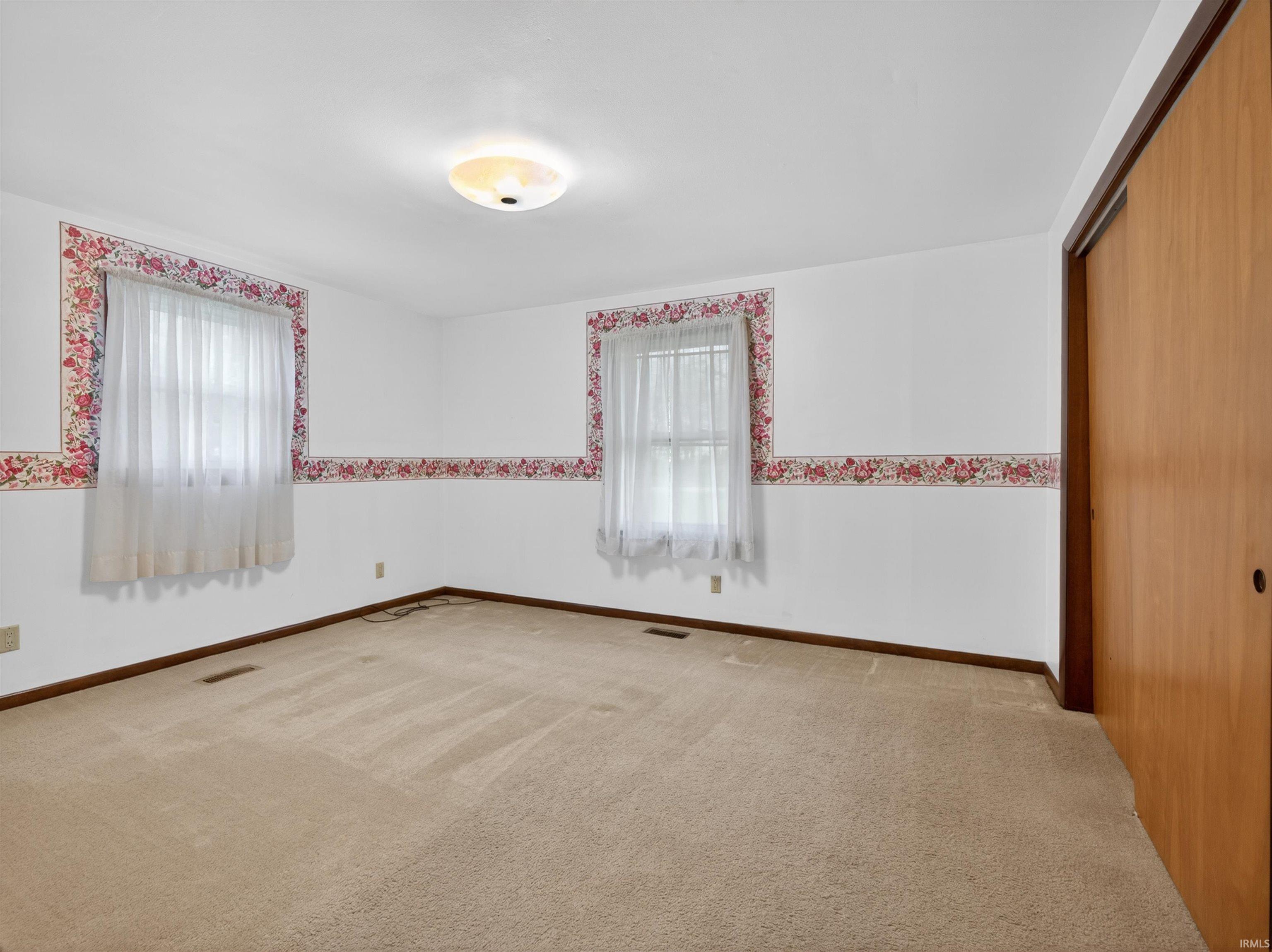 Carpeted interior space featuring two windows with white sheer curtains, a semi-flush ceiling light fixture, and a built-in closet with wood-finish sliding doors