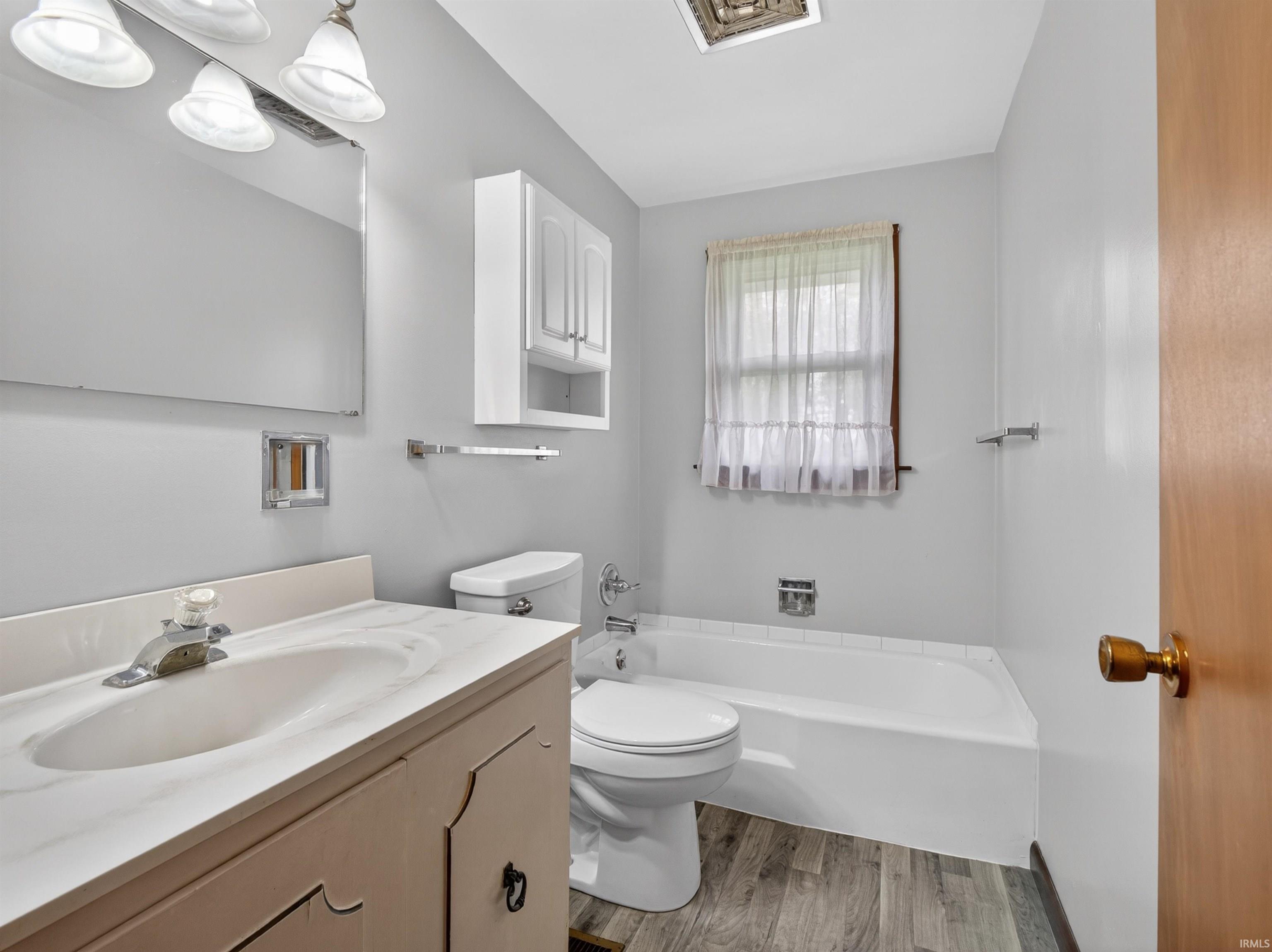Bathroom featuring a vanity with an integrated sink, a built-in bathtub, and wood-finish flooring