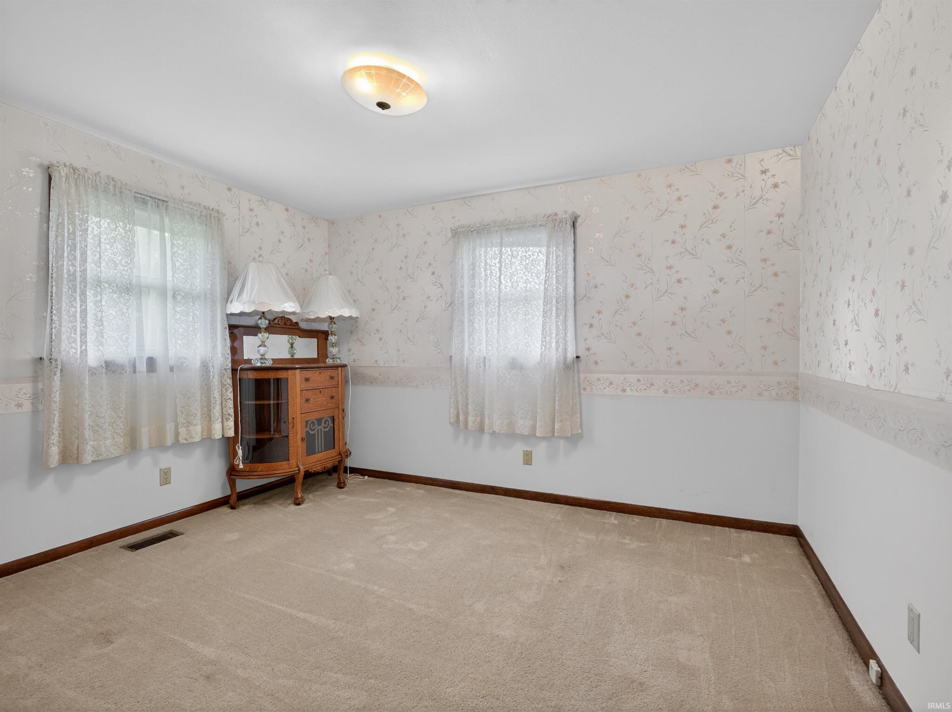 Carpeted interior space featuring dual windows with sheer curtains, a floral pattern wallpaper, and a flush mount ceiling light fixture