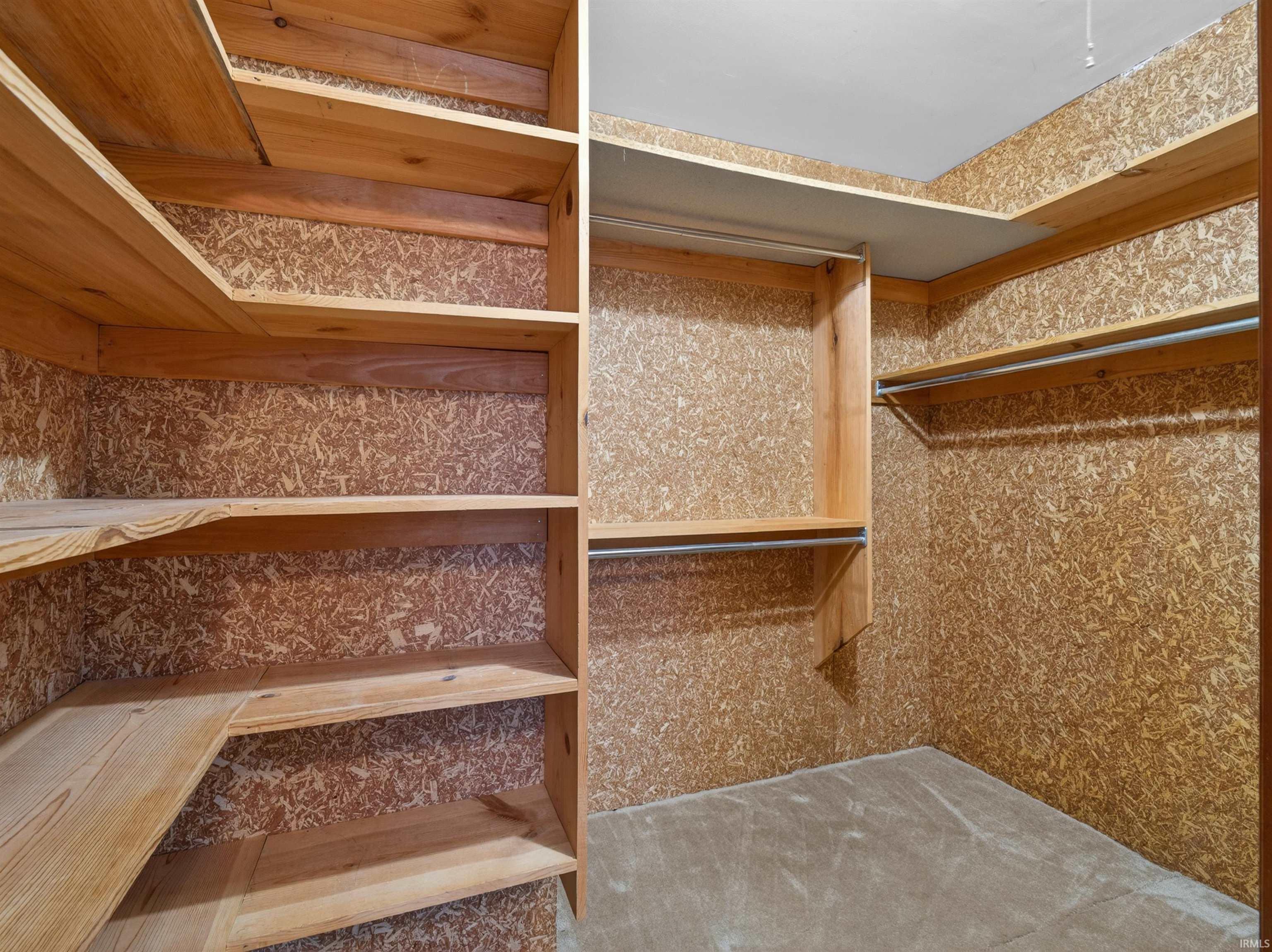 Walk-in closet featuring built-in wood shelving, multiple hanging rods, and a neutral-toned floor