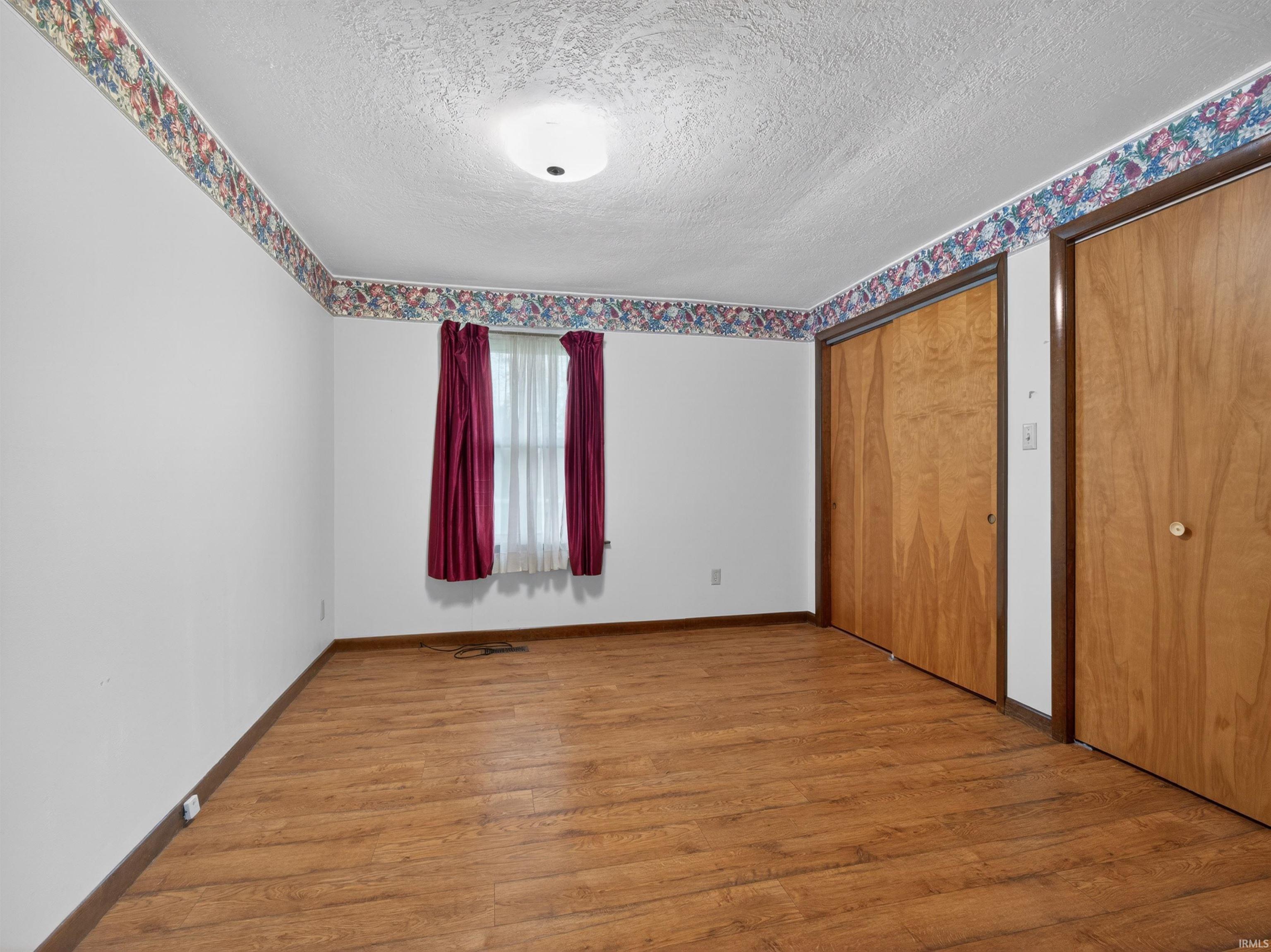 Room featuring light wood-finish flooring, white walls, and a decorative wallpaper border