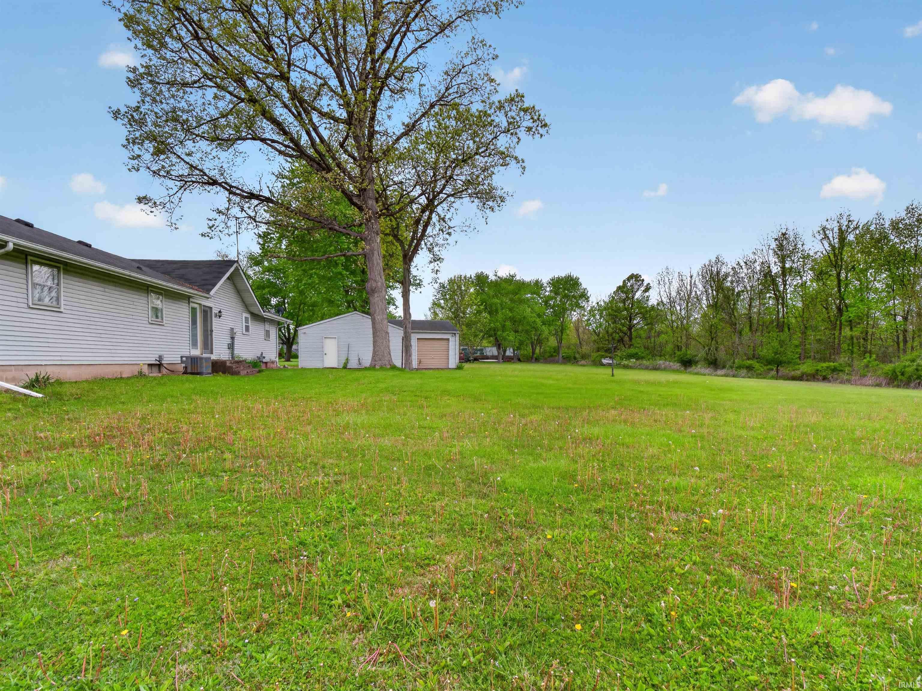 Expansive green lawn with mature trees and a wooded perimeter