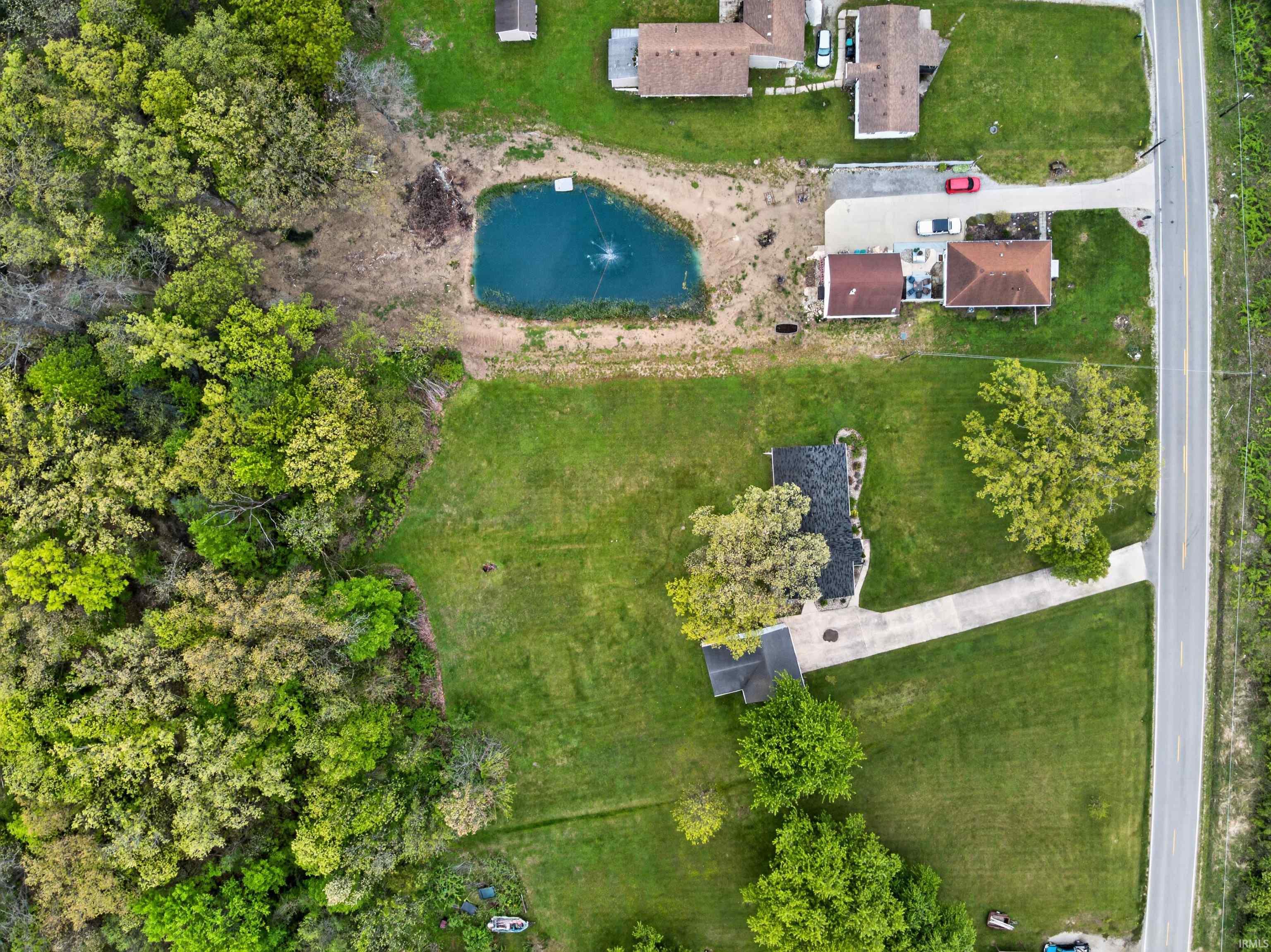 Expansive lot featuring a private pond with a fountain, mature trees, substantial green space, and a paved driveway