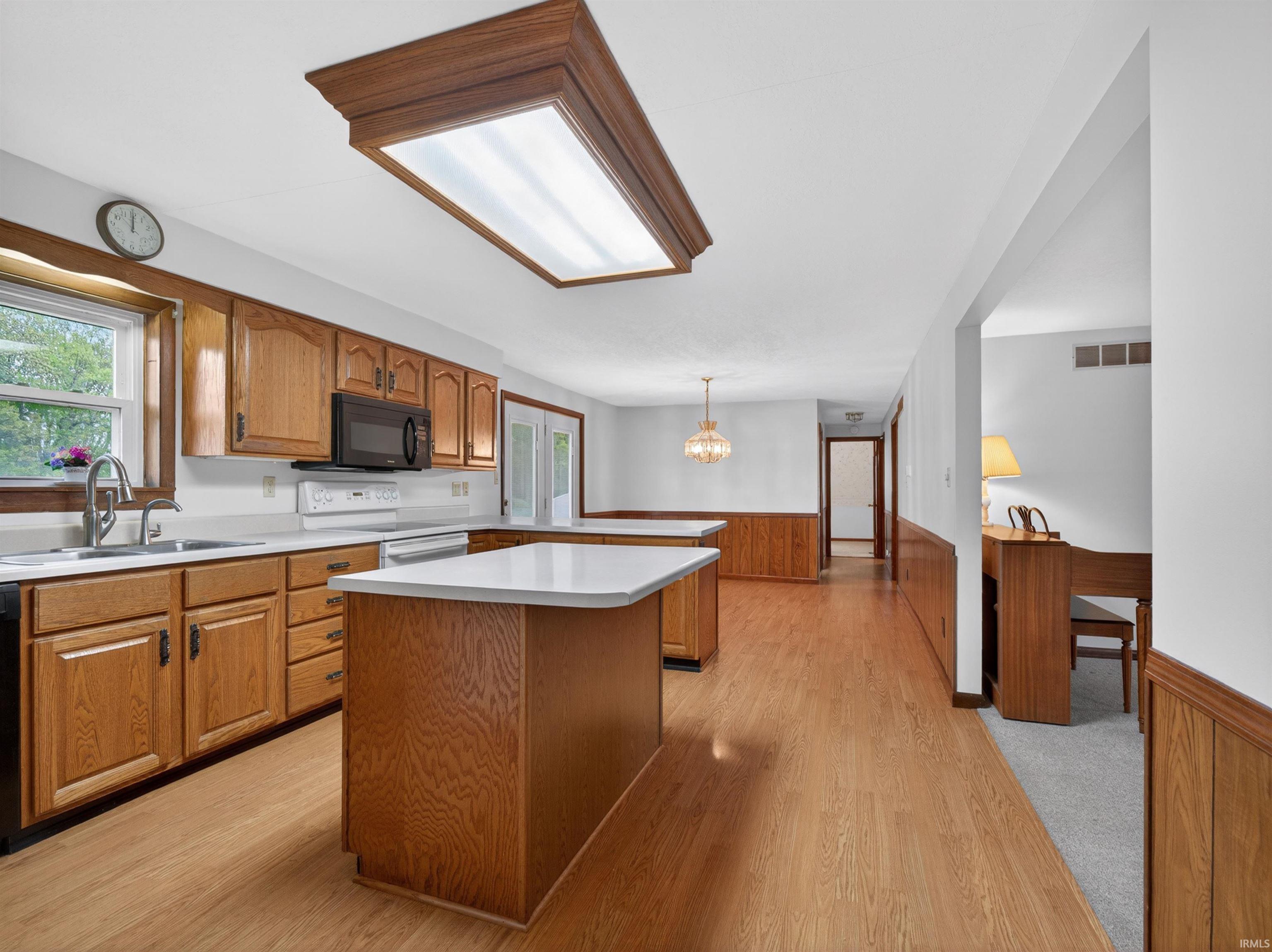 Kitchen featuring two islands with white countertops, light wood-finish cabinetry, built-in microwave, and wood-finish flooring