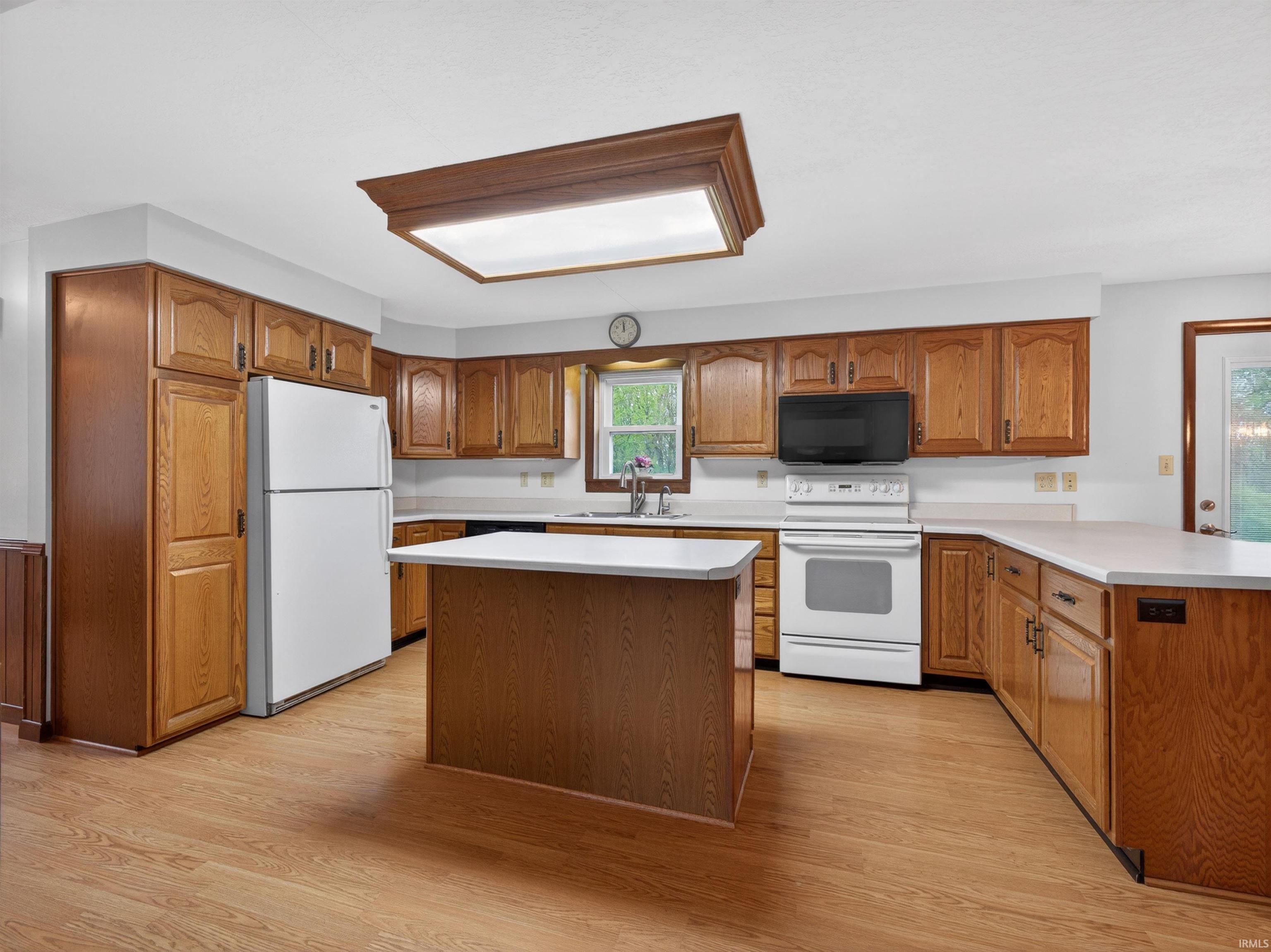 Spacious kitchen featuring wood-finish cabinetry, white countertops, a central island, wood-finish flooring, and white appliances