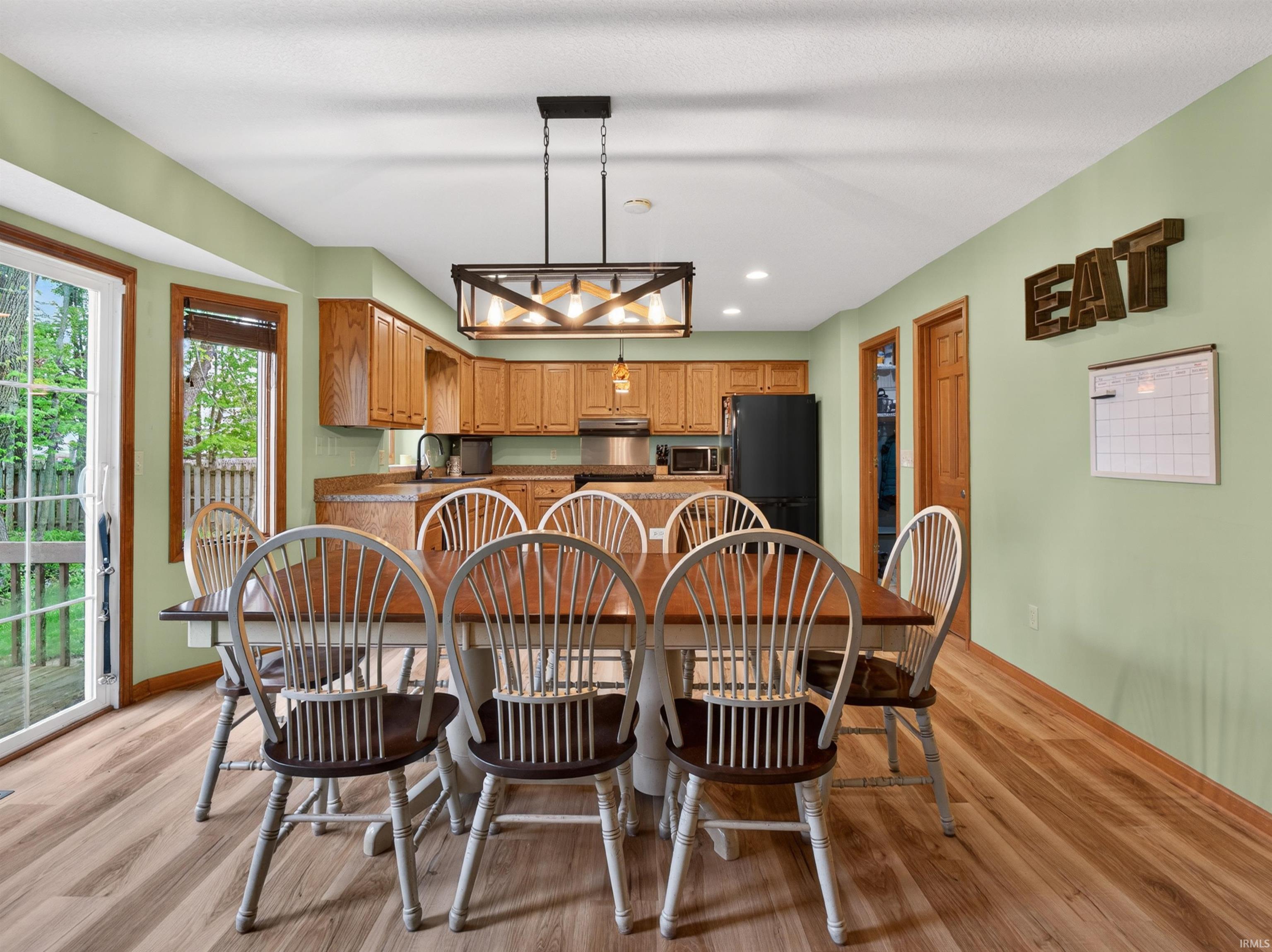 Open-concept kitchen and dining area featuring wood-finish flooring, a contemporary linear chandelier, and wood cabinetry