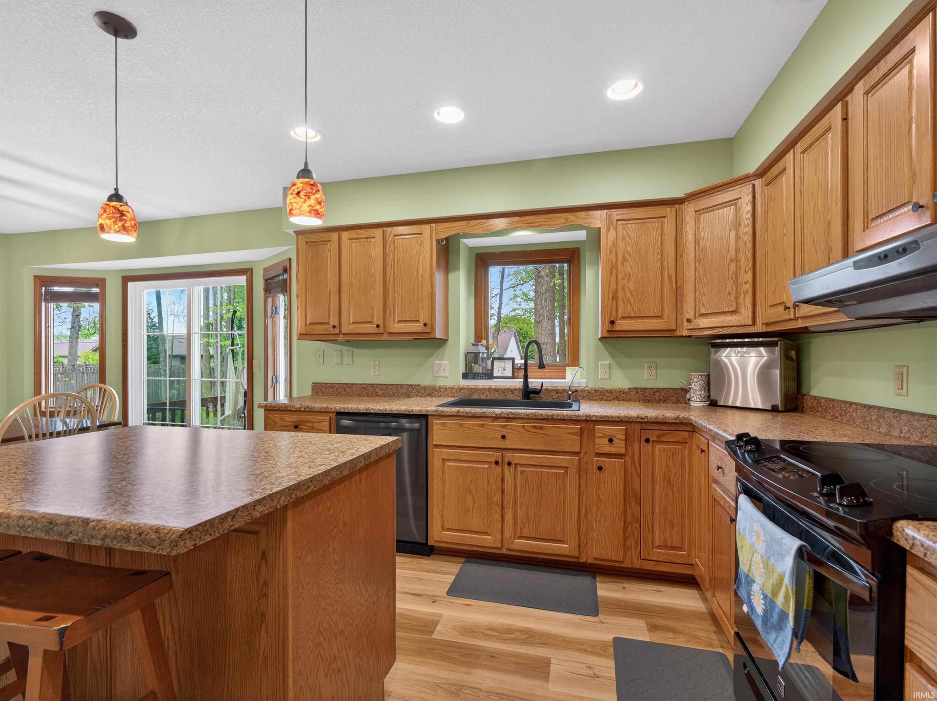 Open-concept kitchen featuring wood-finish cabinetry, granite-style countertops, wood-finish flooring, and a stainless steel sink with a black faucet