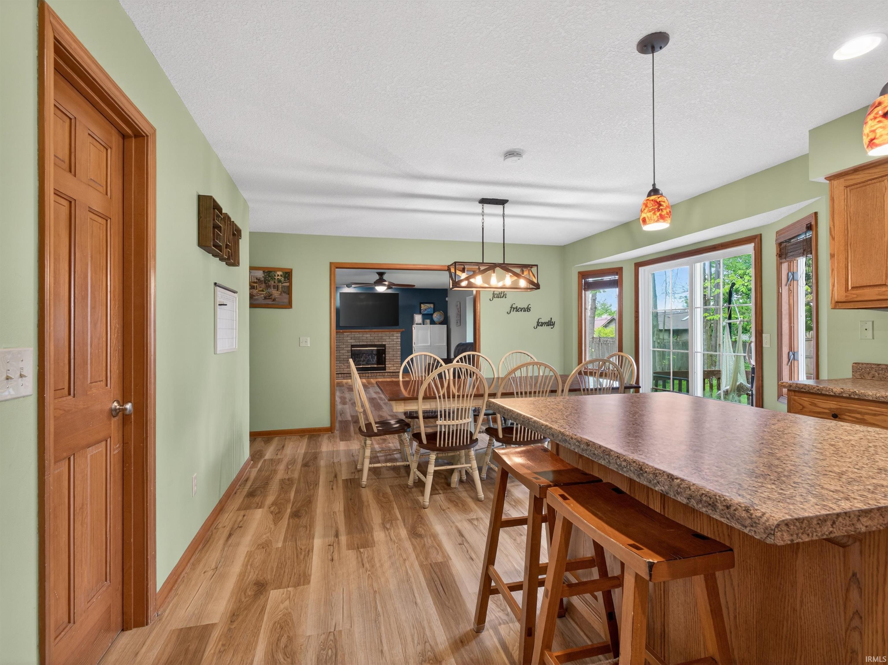 Kitchen and dining area featuring wood-finish flooring, a breakfast bar with stone-finish countertop, pendant lighting, and abundant natural light from multiple windows and a sliding glass door