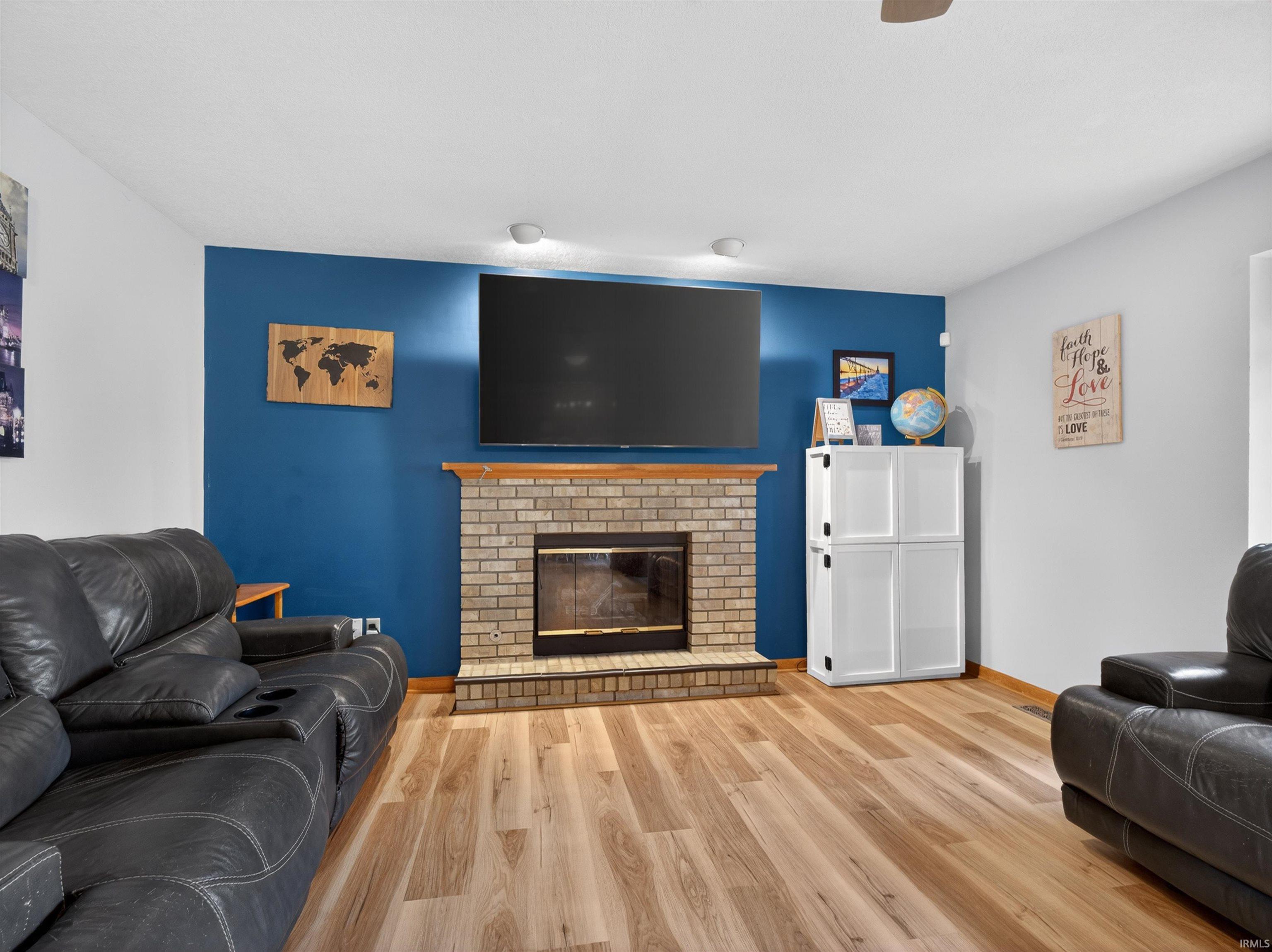 Living area featuring a brick fireplace with a wood mantle, wood-finish flooring, and a ceiling fan