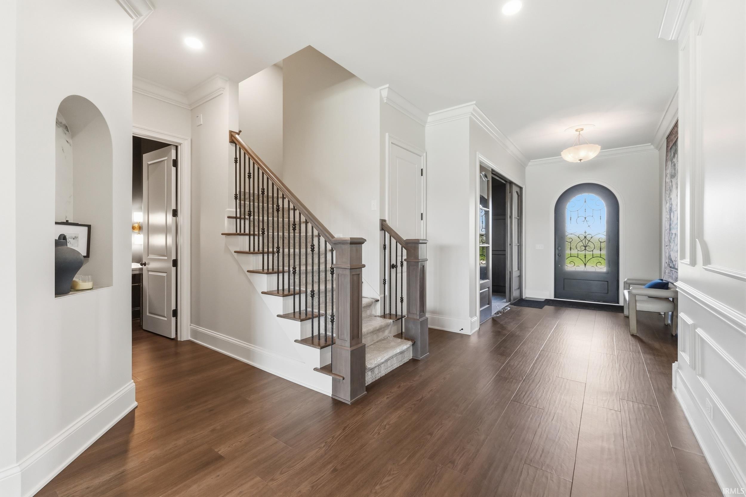 Foyer featuring dark wood-finish flooring, an arched entry door with decorative glass, and a grand staircase with dark wood handrails and wrought iron balusters