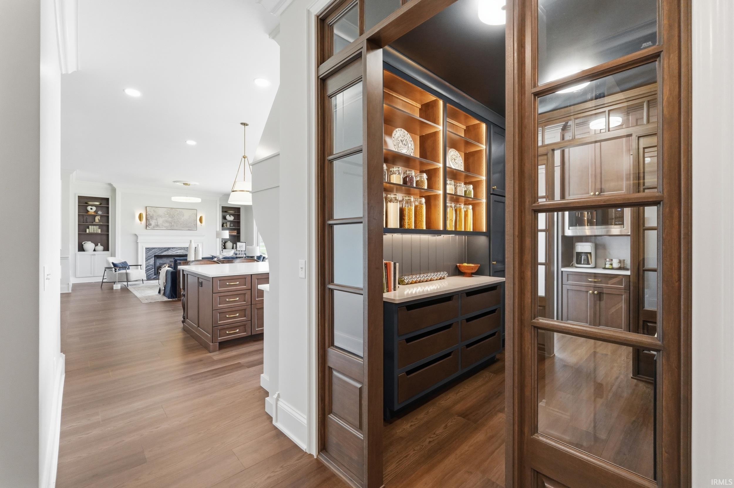 Custom pantry featuring glass-paneled doors, wood-finish shelving with integrated lighting, a substantial countertop, and built-in drawers