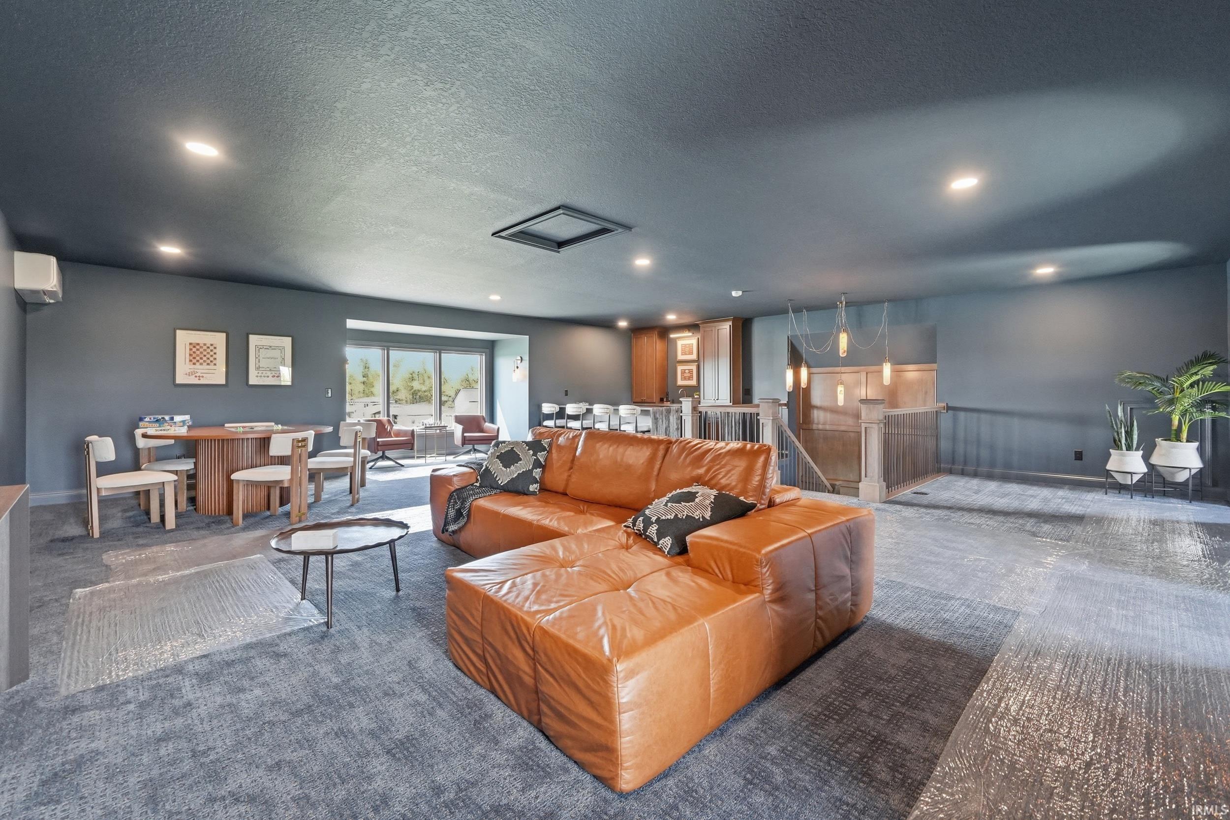 Spacious room with dark gray walls and ceiling, featuring recessed lighting, gray patterned carpeting, and a built-in wet bar with wood cabinetry