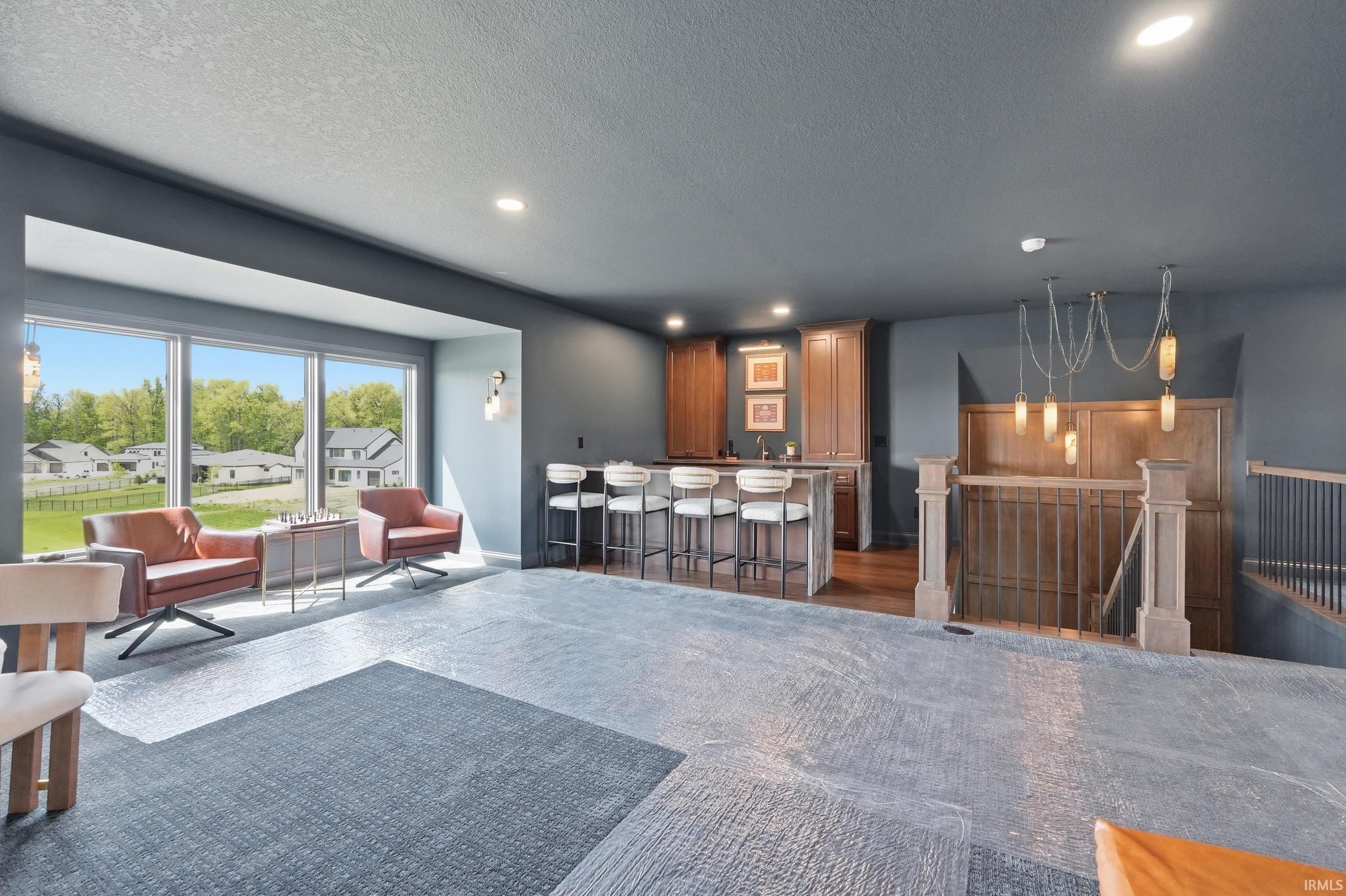 Full-height windows with a deep sill, built-in wet bar with wood-finish cabinetry, recessed lighting, stylish hanging light fixture, and a staircase featuring wood newel posts and metal balusters