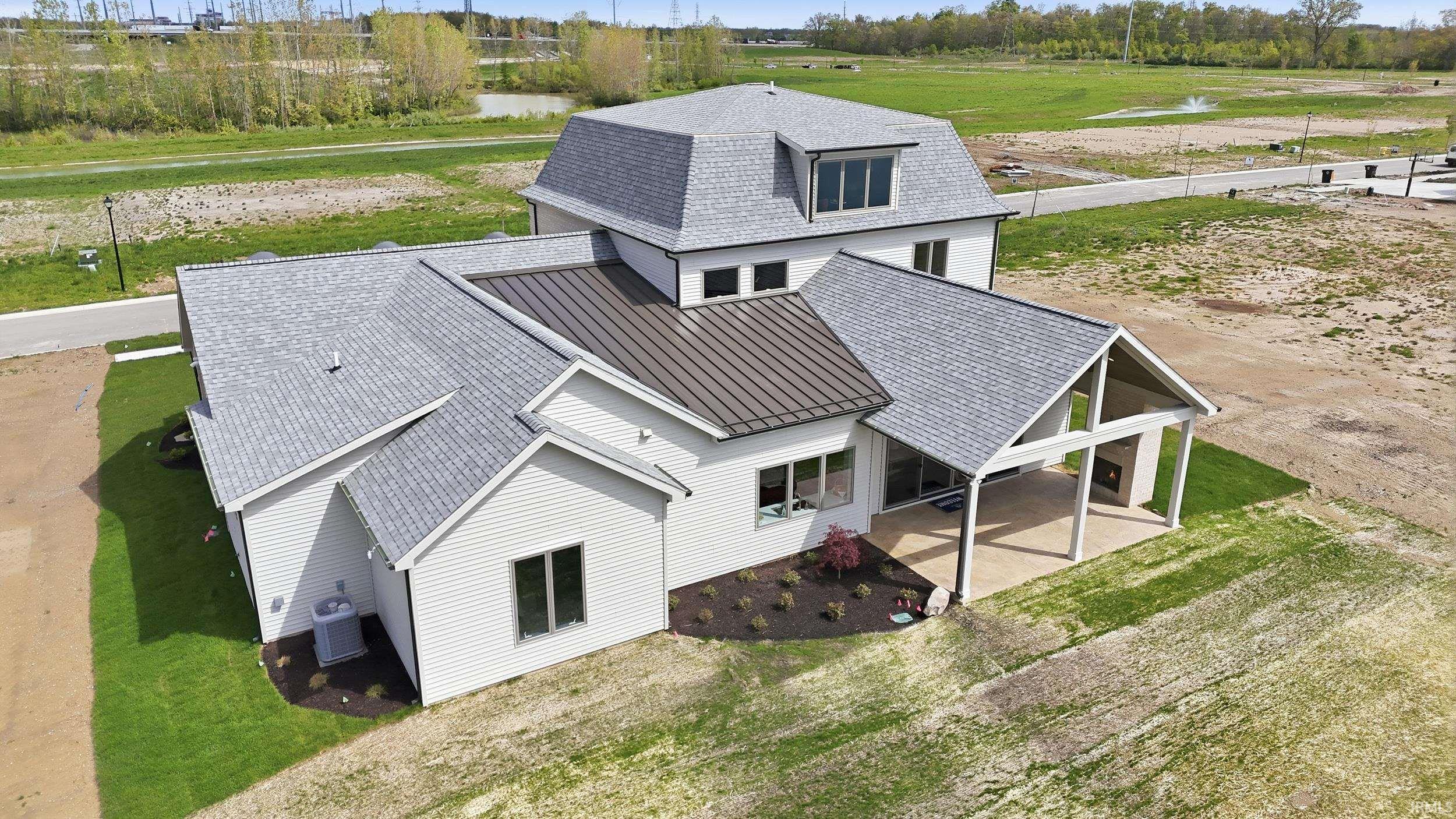 Contemporary residence featuring a light-colored exterior, multiple rooflines including a standing seam metal roof, a large covered patio with an outdoor fireplace, and a dormered upper level