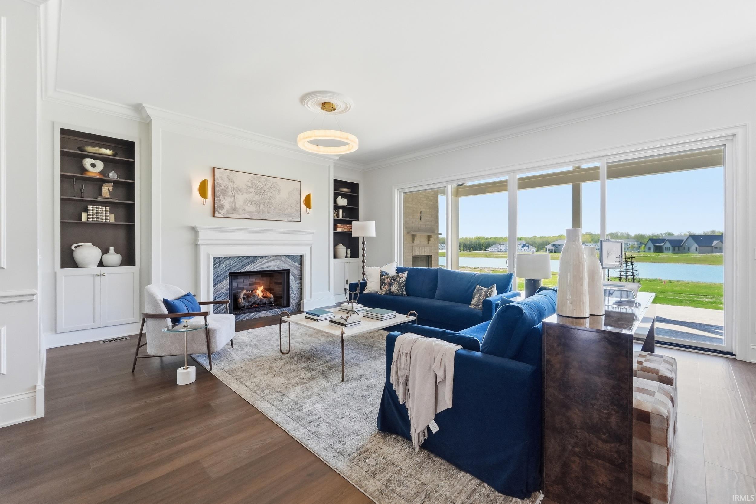 Spacious living area featuring wood-finish flooring, a white mantel fireplace with a stone surround, built-in shelving, crown molding, and expansive sliding glass doors