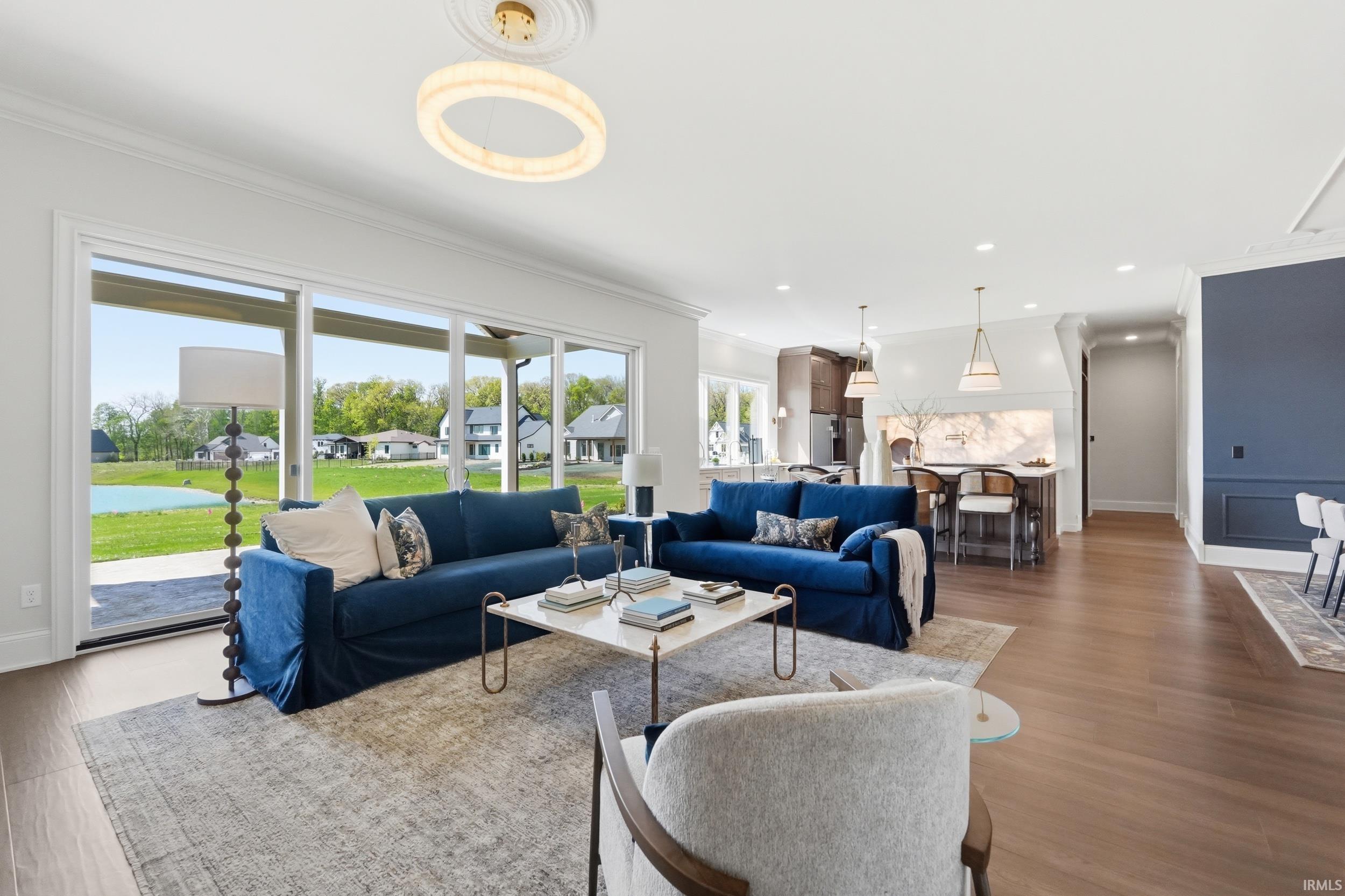 Spacious living area featuring expansive glass sliding doors, wood-finish flooring, recessed lighting, crown molding, and a modern circular ceiling fixture