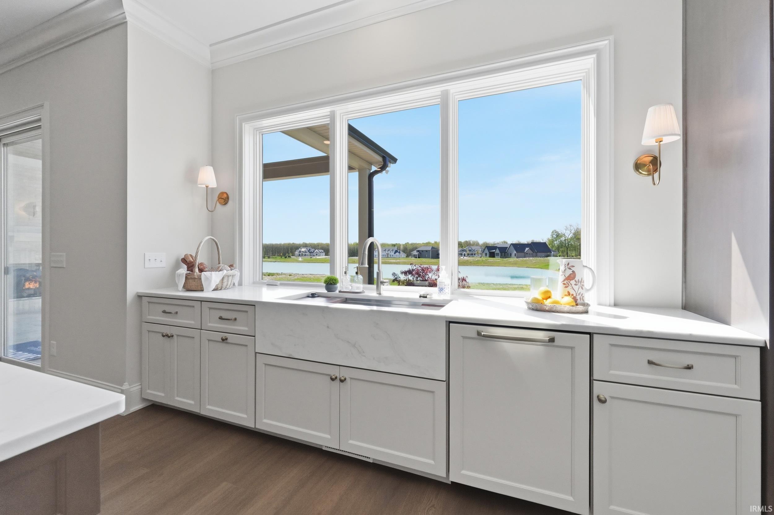 Kitchen workstation featuring a wide window, undermount farmhouse sink, light cabinetry, white countertops, and wood-finish flooring