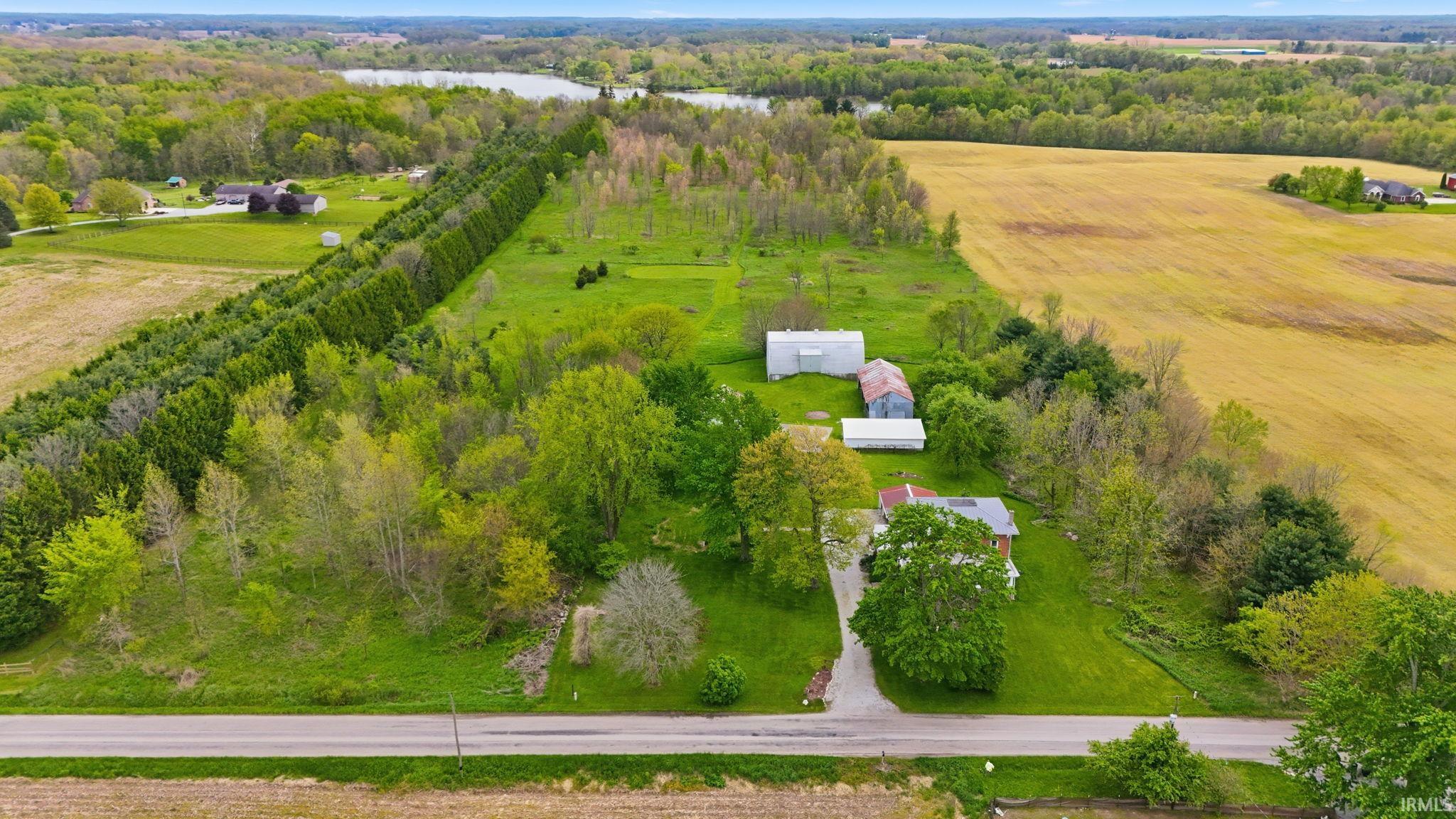 Expansive property featuring a red-roofed residence, multiple outbuildings, and a gravel driveway