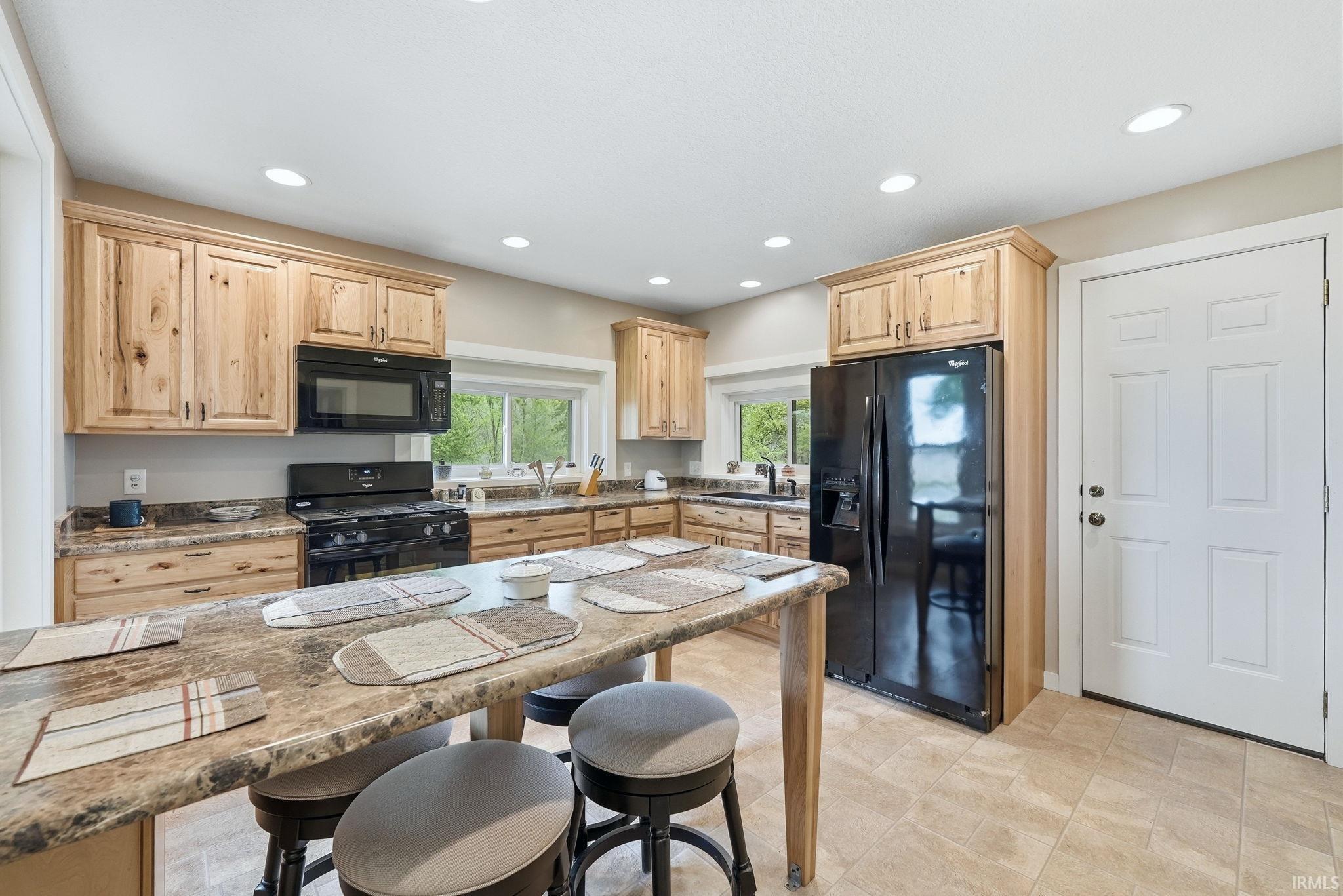 Kitchen featuring a central island with seating, natural wood cabinetry, black appliances including a refrigerator, range, and built-in microwave, and recessed lighting