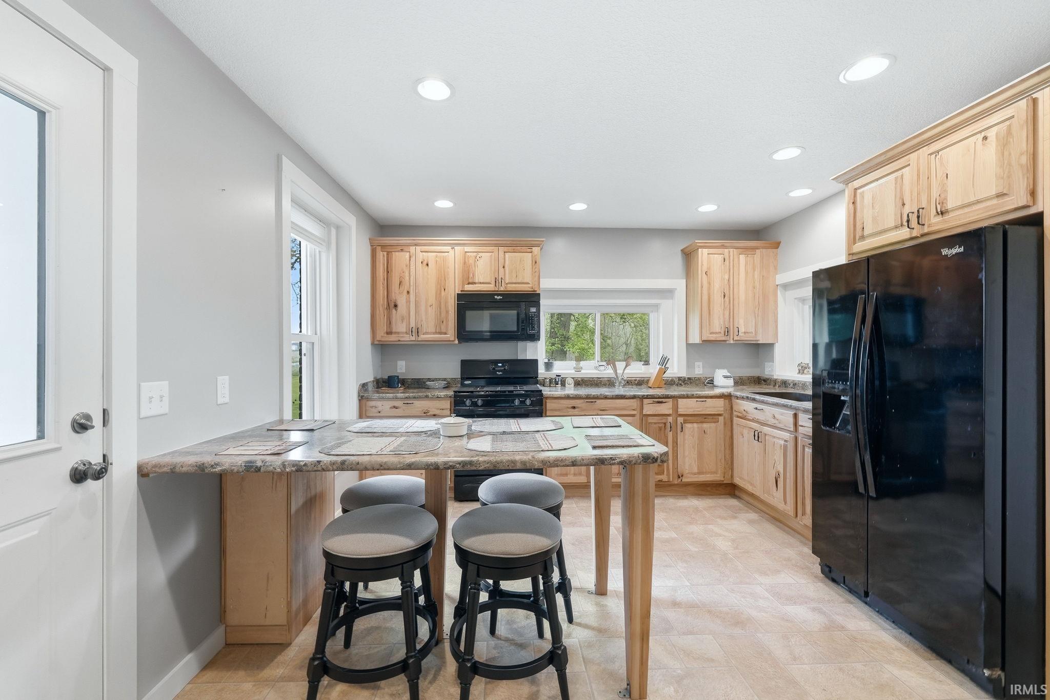 Kitchen featuring light wood cabinetry, stone-finish countertops, and black appliances