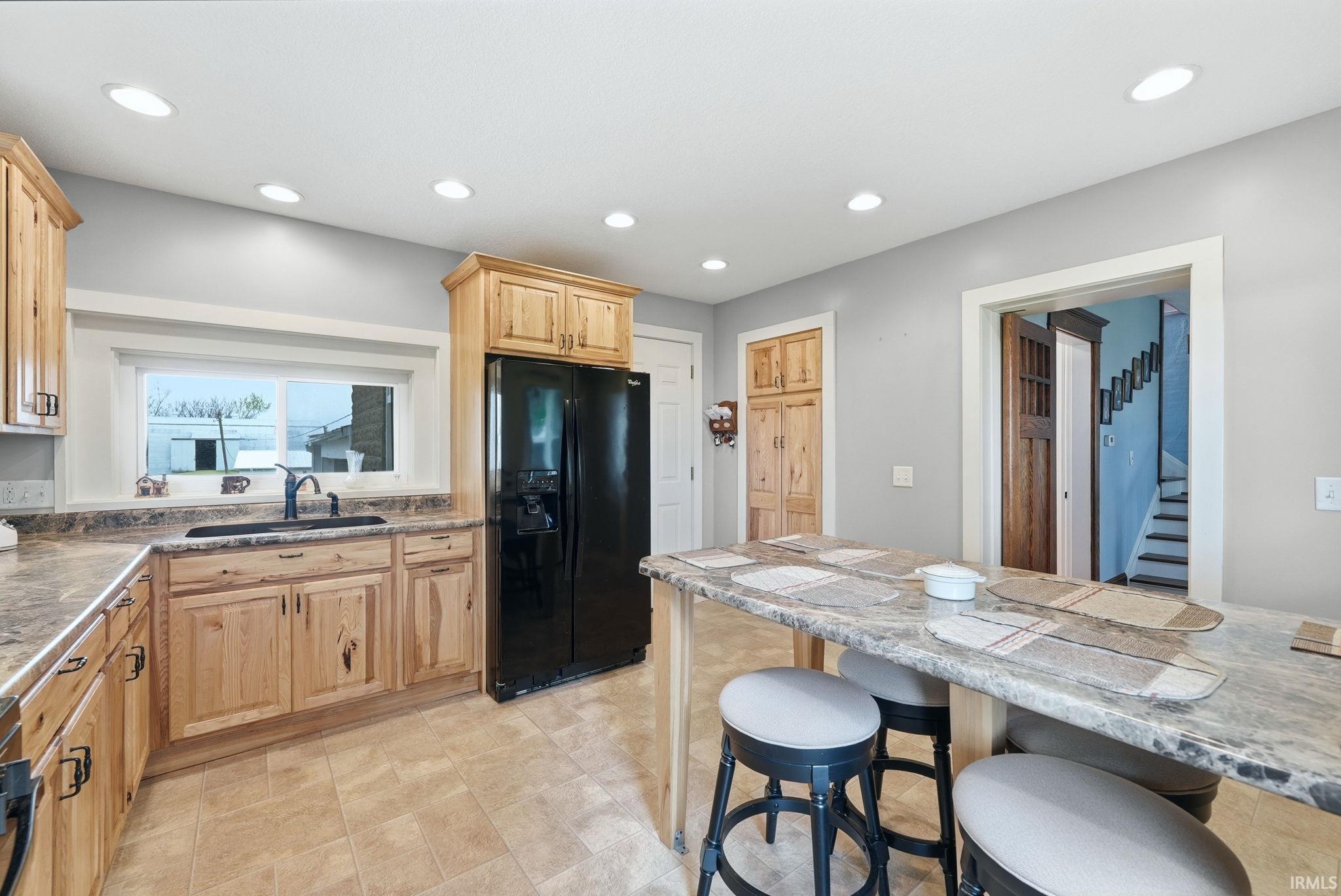 Kitchen featuring wood-finish cabinetry, a black refrigerator, recessed lighting, and a kitchen island with seating