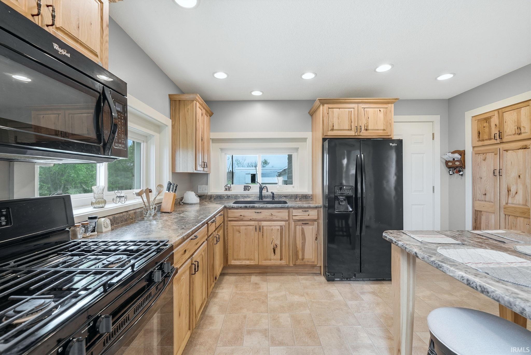 Kitchen featuring wood-finish cabinetry, black appliances, recessed lighting, and a countertop island