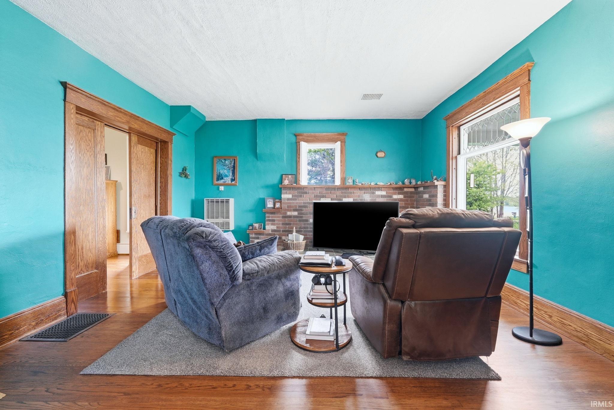 Living area featuring wood-finish flooring, a brick fireplace, pocket doors with wood trim, and large windows