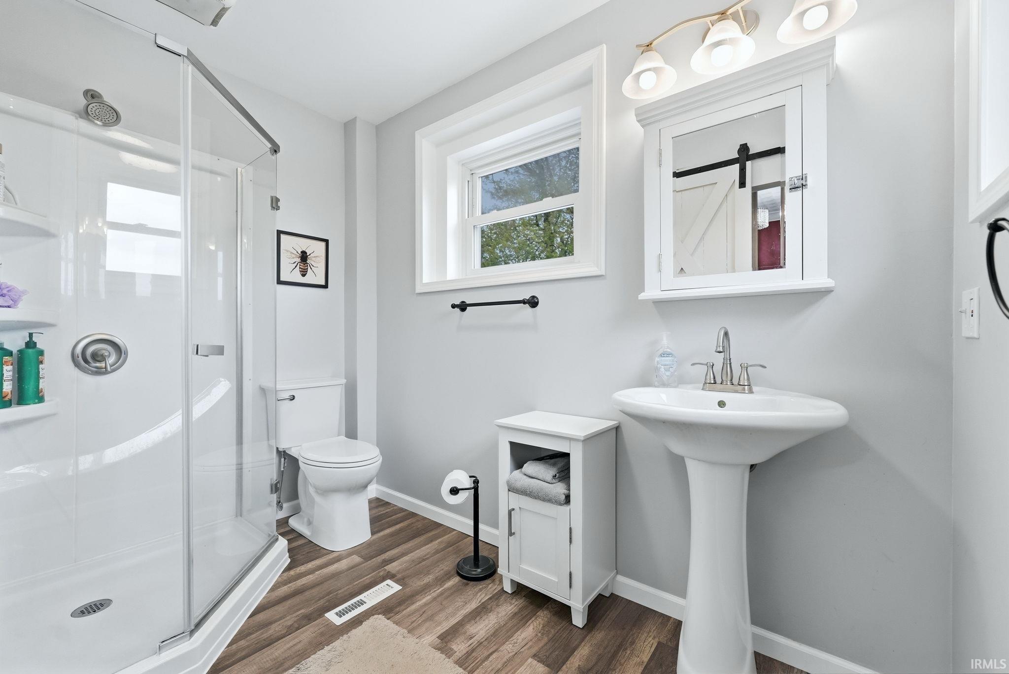 Bathroom featuring a clear glass shower enclosure, white pedestal sink, and wood-finish flooring