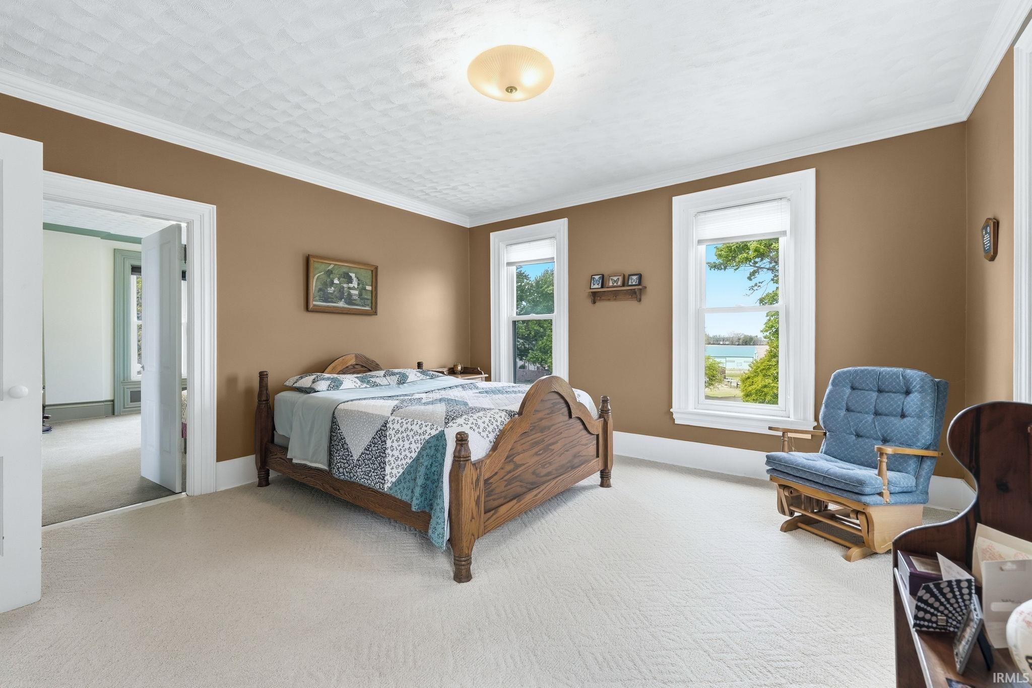 Bedroom featuring two large windows with water and treeline scenery, neutral wall color, white crown molding, and light-colored patterned carpeting